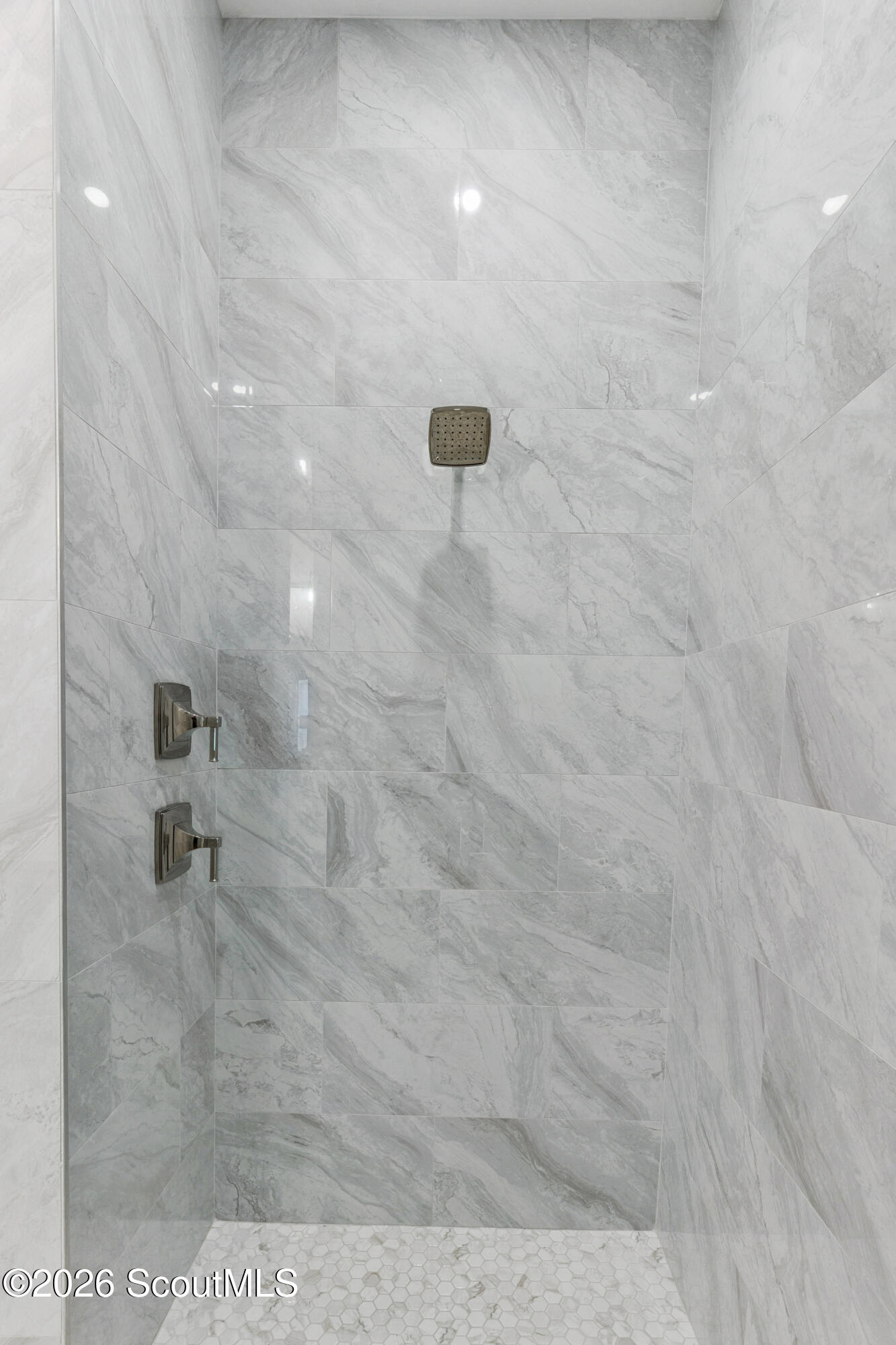 Walk-in shower with gray veined tile, dark metal controls, and a white hexagonal mosaic floor.