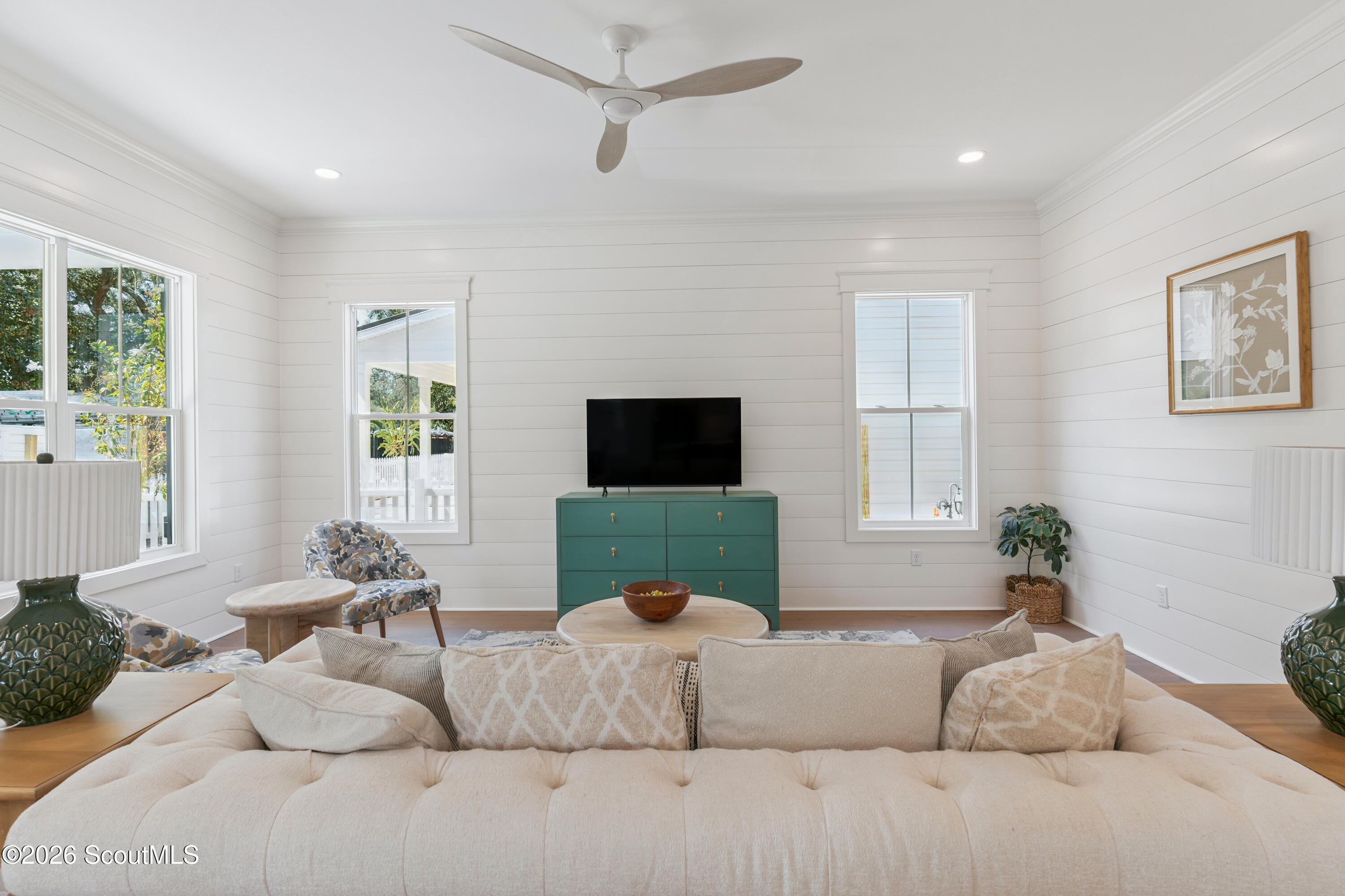 Bright living room with white shiplap walls, cream sofa, and green dresser beneath a television.