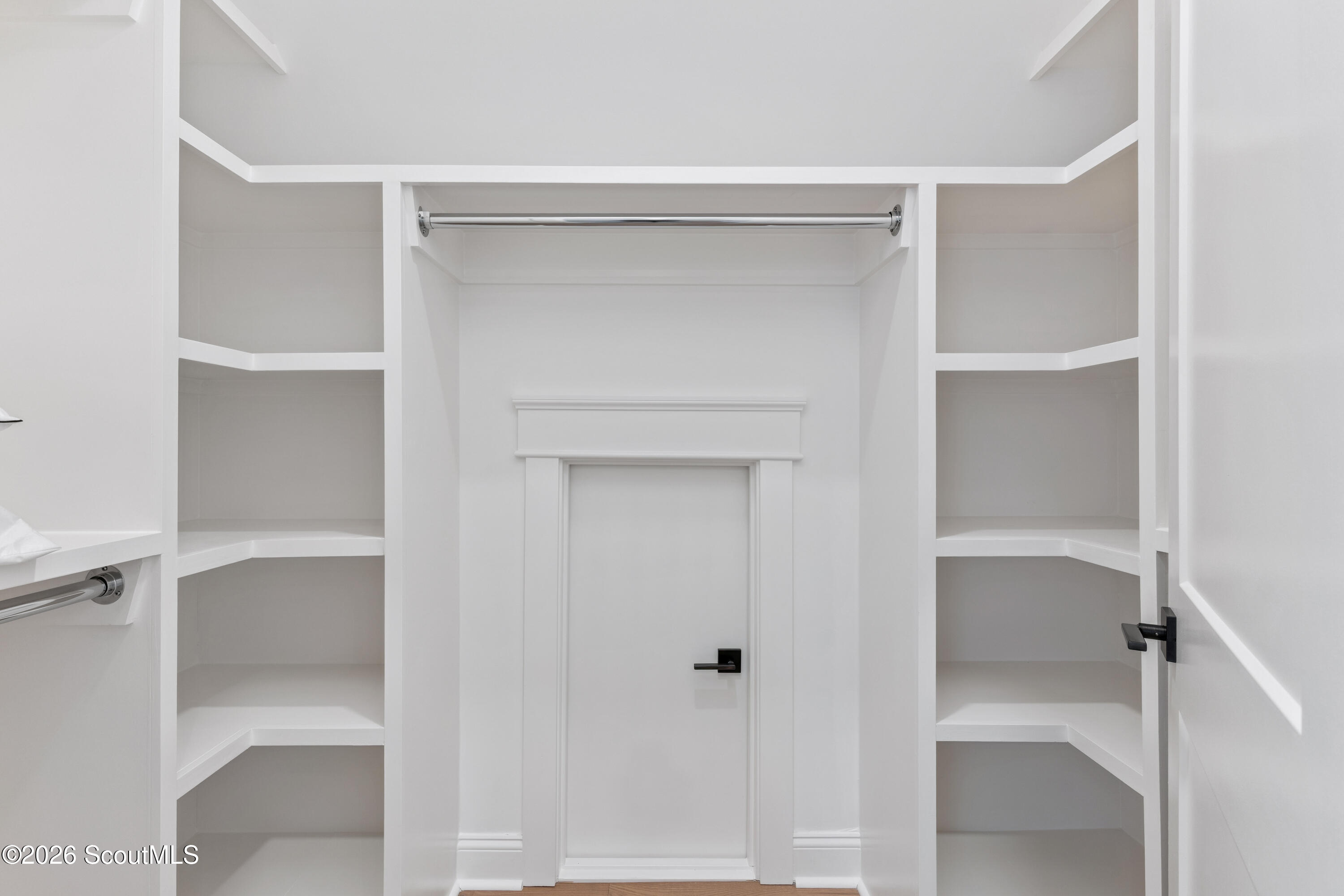 Walk-in closet with white built-in shelves, a chrome hanging rod, and a paneled door.