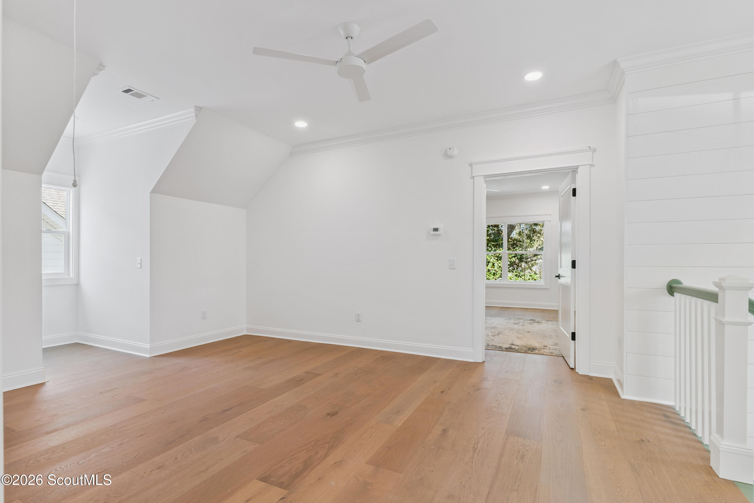 Empty upper-level room with wide-plank wood floors, a ceiling fan, and a stair railing.