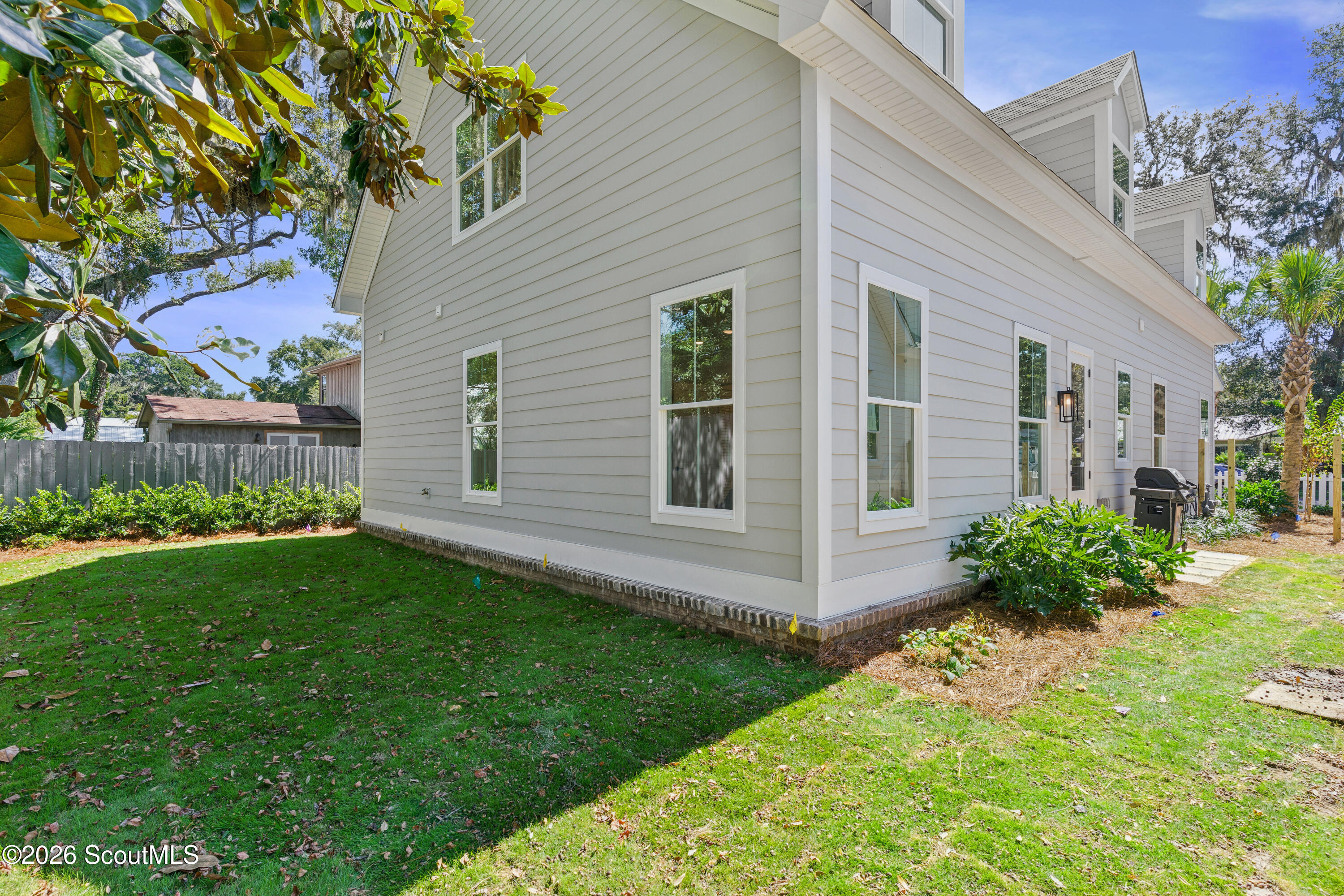 Light-colored house with multiple gables, white-trimmed windows, and a landscaped lawn.