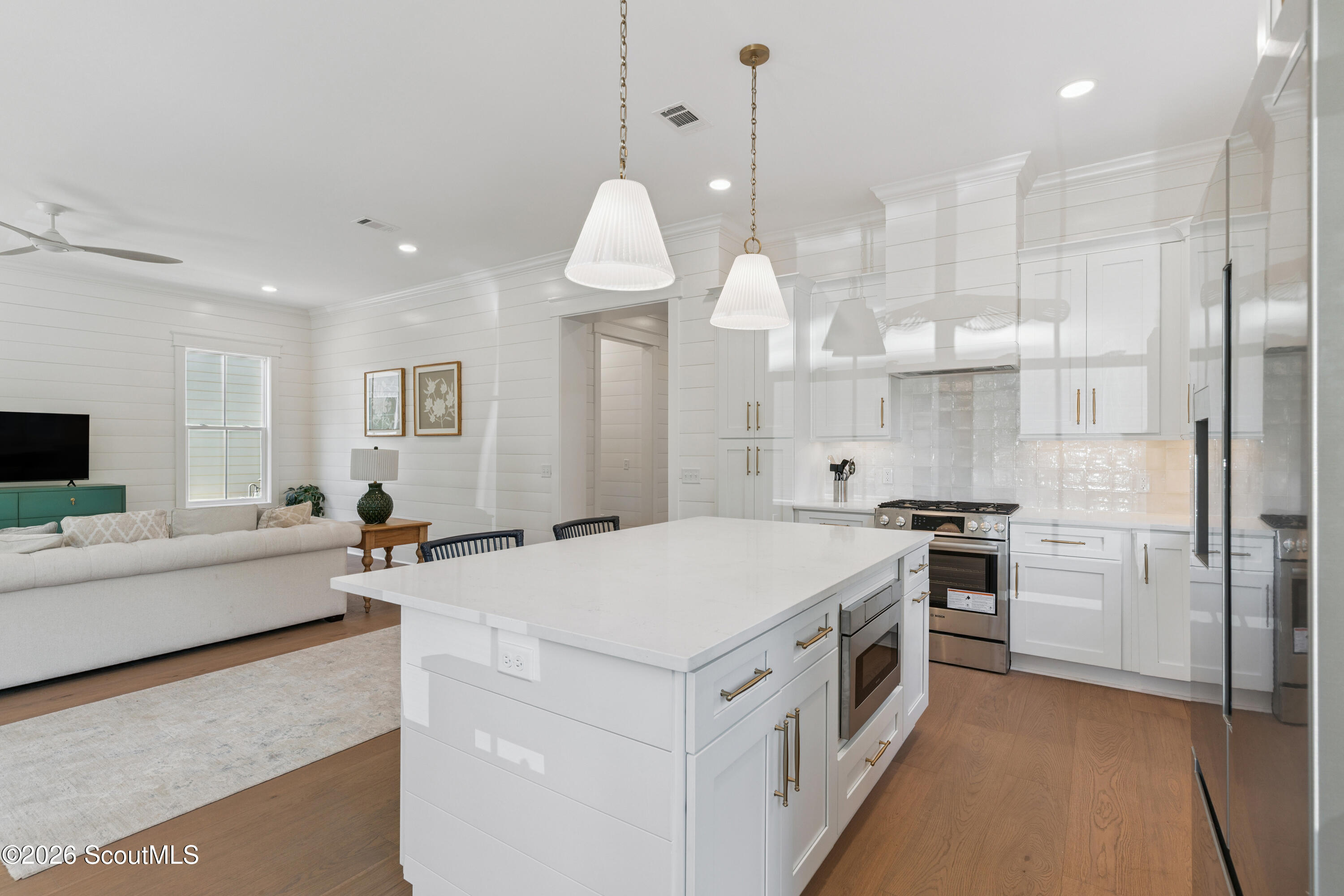 Open-plan kitchen with a large white island, stainless steel appliances, and an adjoining living area.