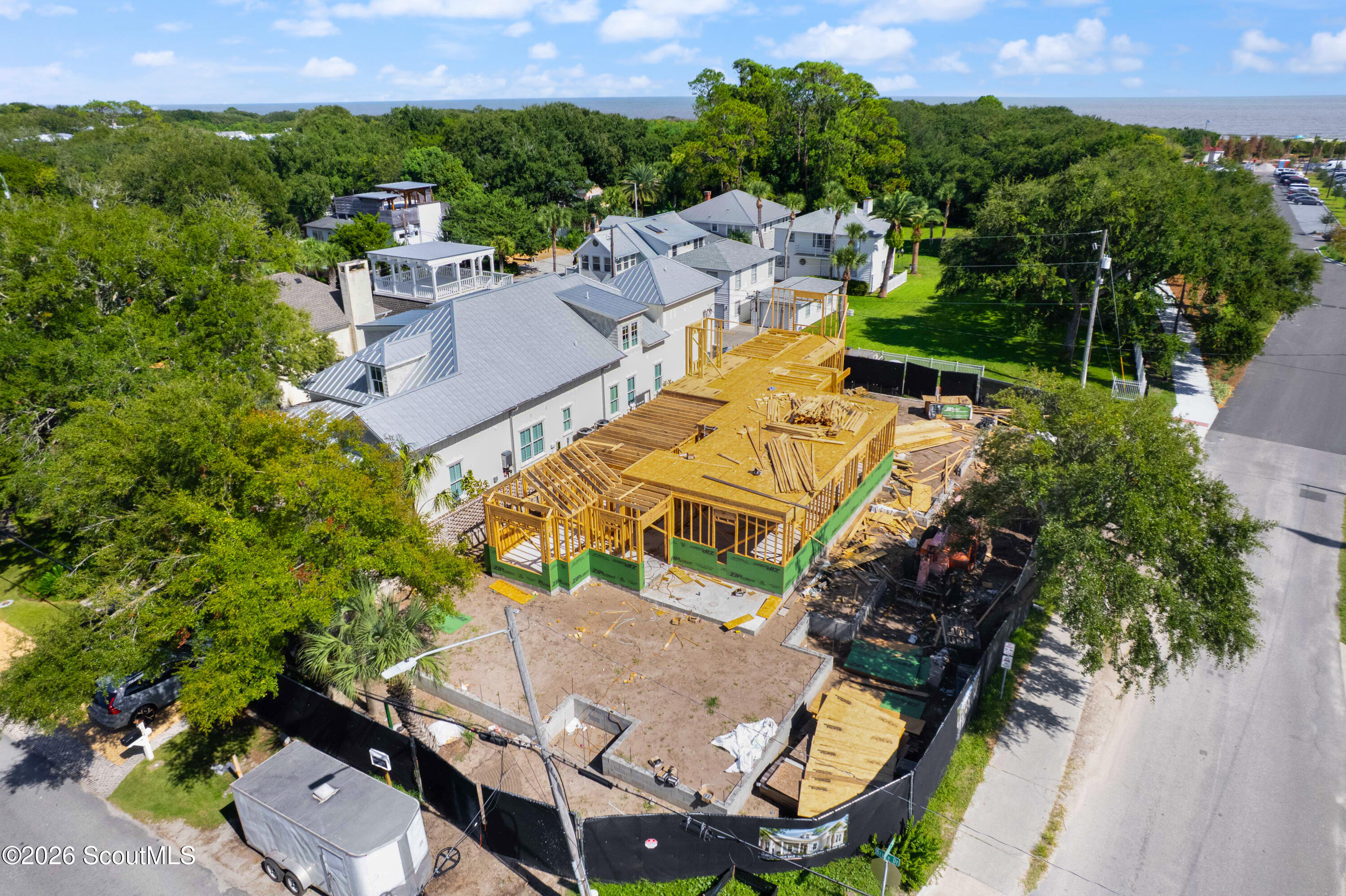 Aerial view of a coastal home under construction, with exposed framing and the ocean in the distance.