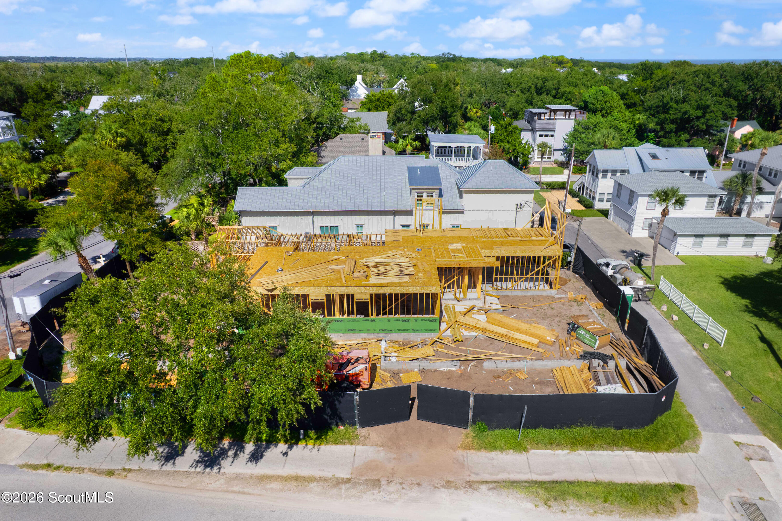 Aerial view of a house under construction, with exposed timber framing and a tree-lined neighborhood.