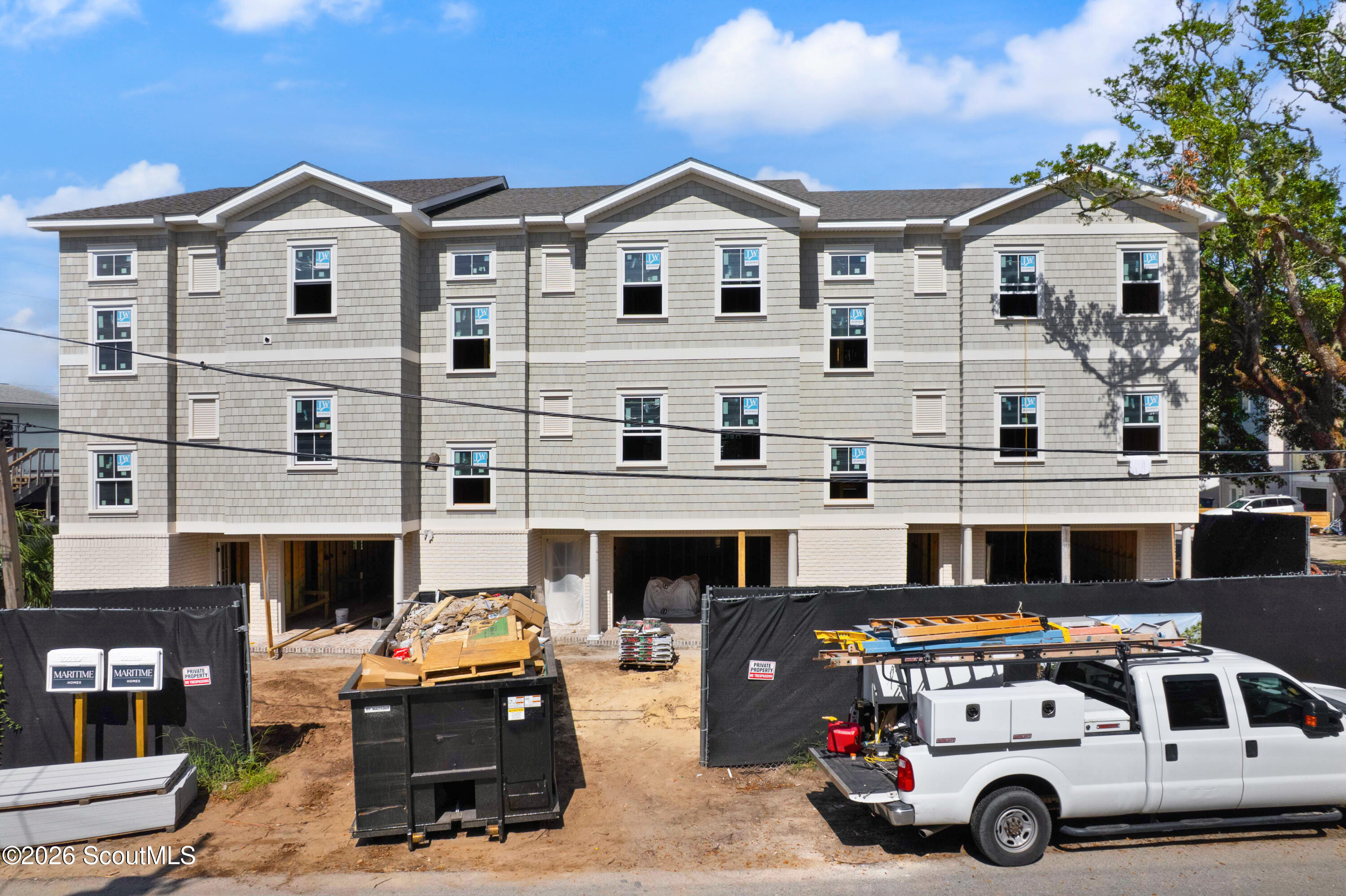 Three-story shingle-sided residential building under construction, with a work truck and construction materials.