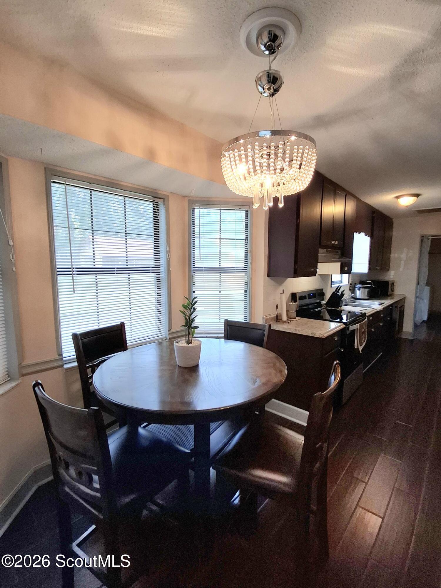 Dining area with a round table beneath a crystal chandelier, opening to a dark-cabinet kitchen.