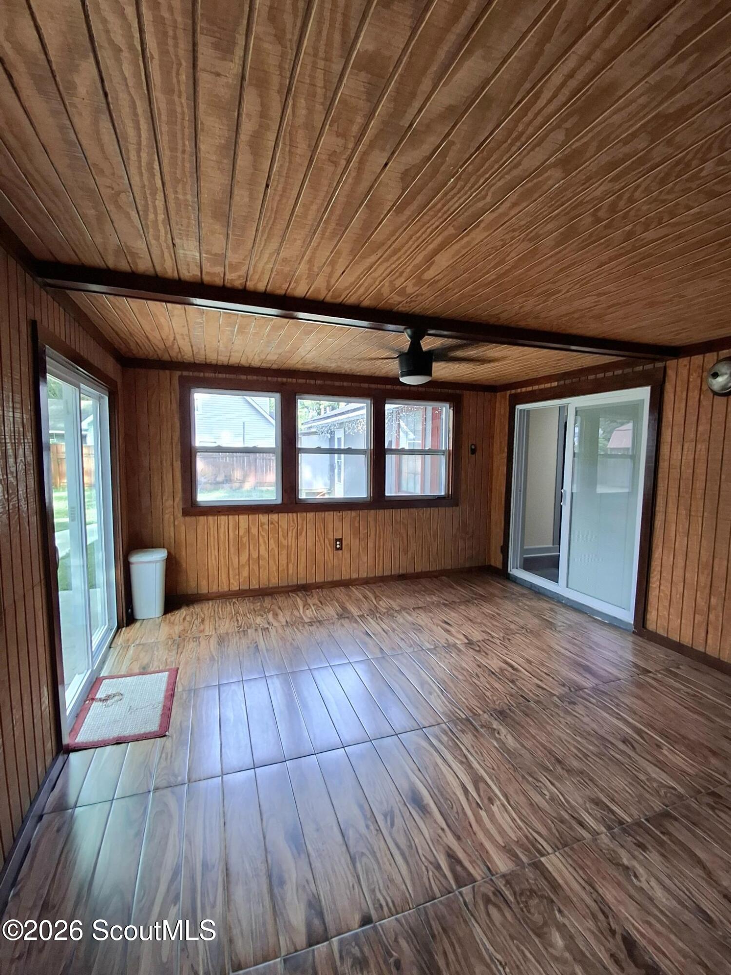 Empty wood-paneled sunroom with a wood-plank ceiling, tile floor, and sliding glass doors.