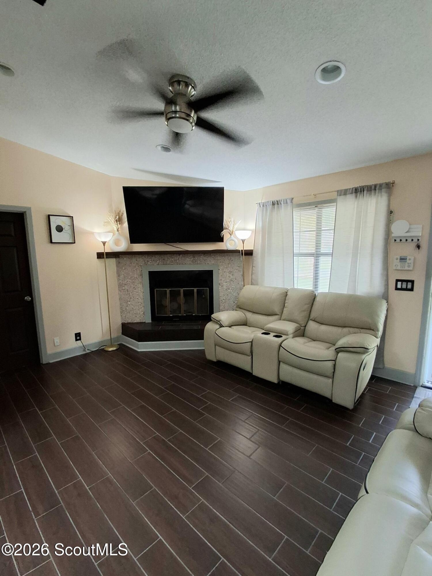 Living room with a stone fireplace, wall-mounted TV, reclining sofa, and dark tile flooring.