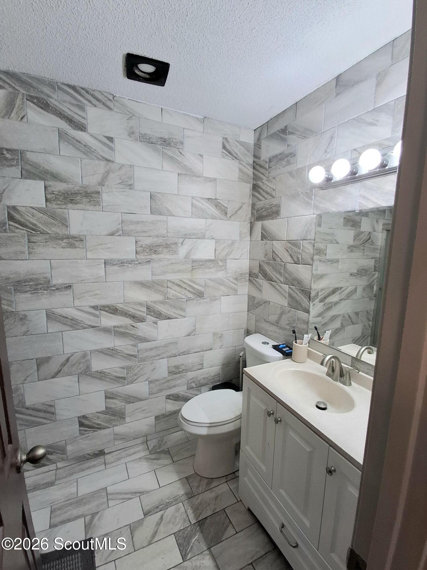Bathroom with gray-and-white tiled walls, a white vanity, and a toilet.