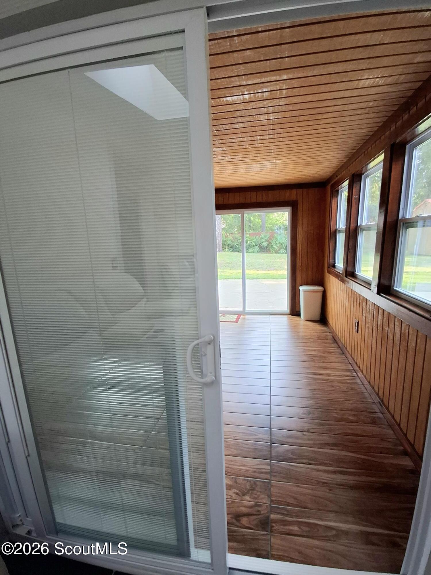 Enclosed sunroom with wood-paneled walls, wood-look tile flooring, and windows overlooking the yard.