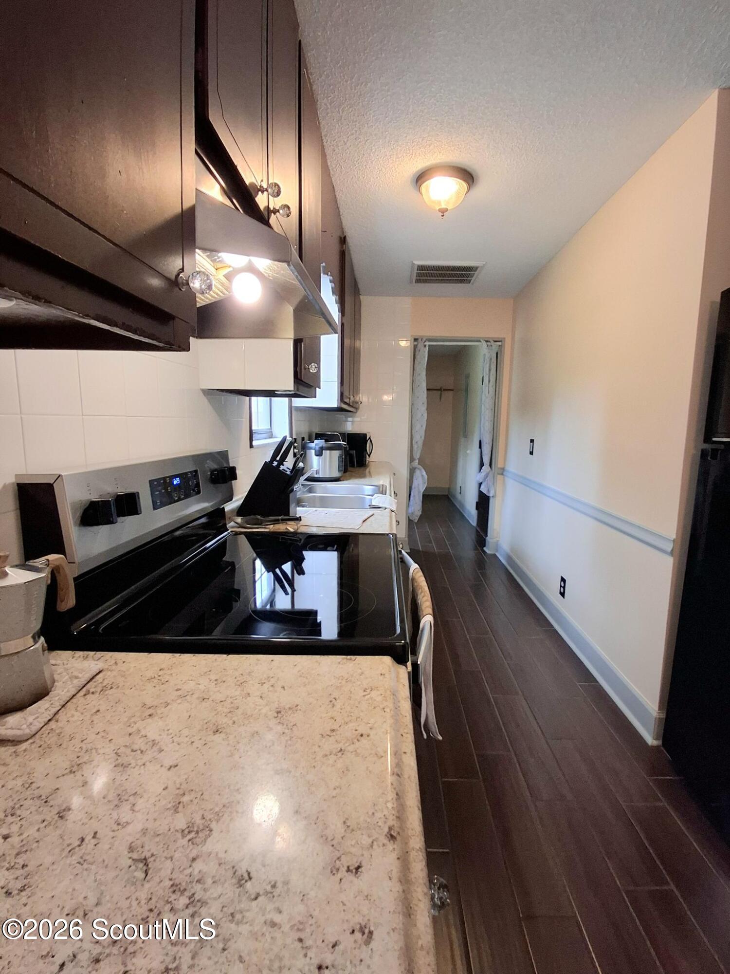 Narrow galley kitchen with dark cabinets, speckled stone counters, and dark plank flooring.