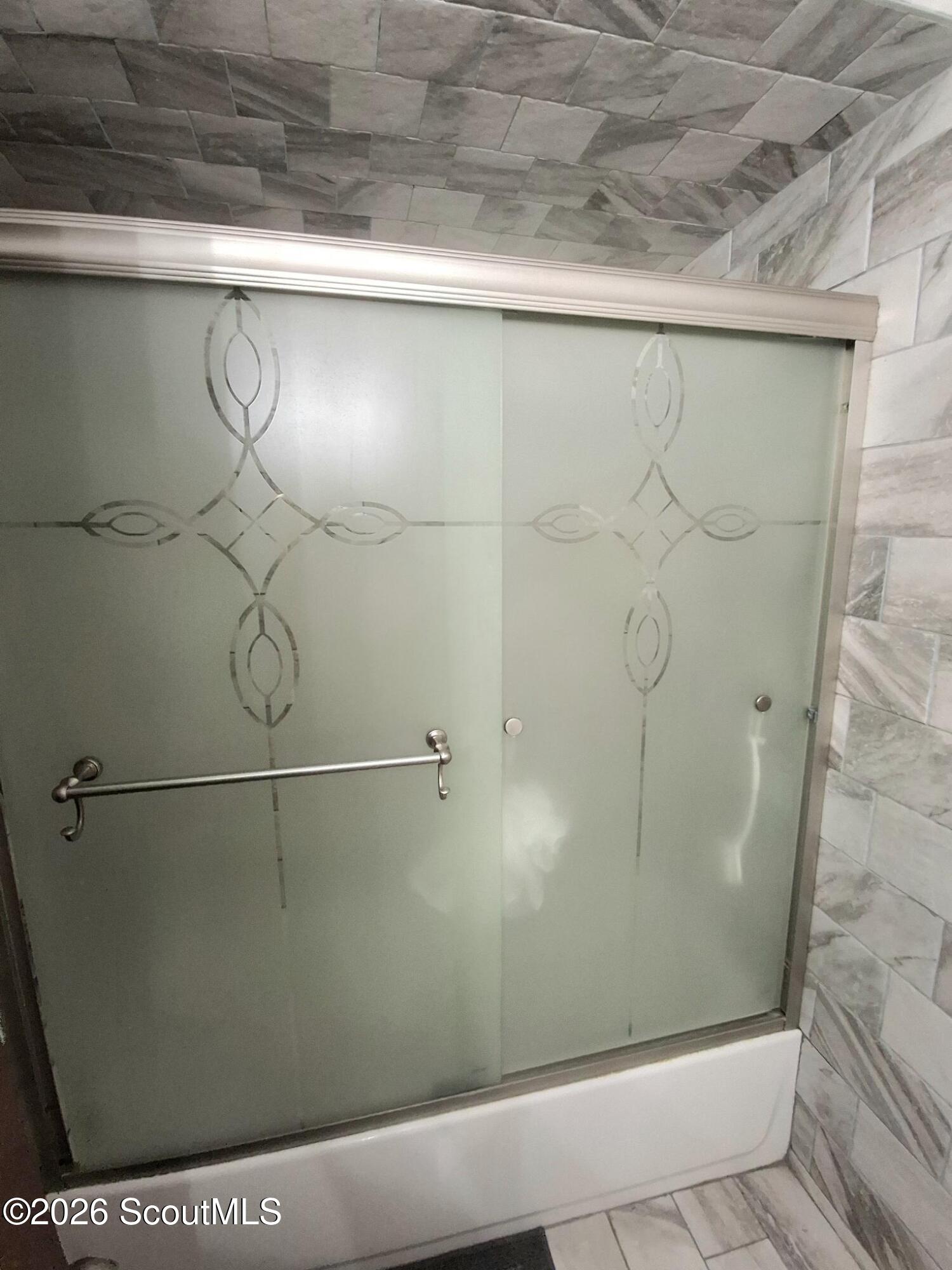 Bathtub with patterned frosted-glass sliding doors and gray marble-look tile.