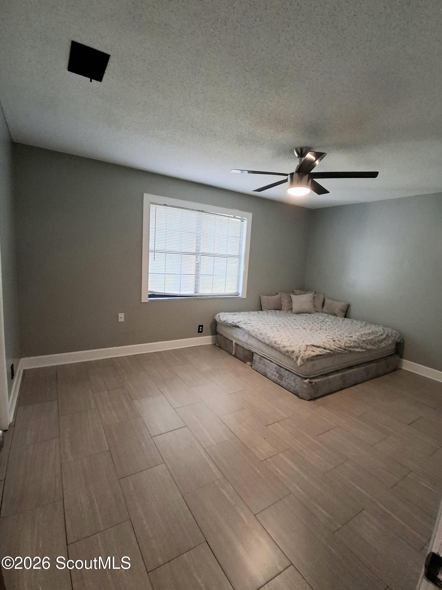Bedroom with a low bed, gray walls, tiled floor, and a ceiling fan with light.
