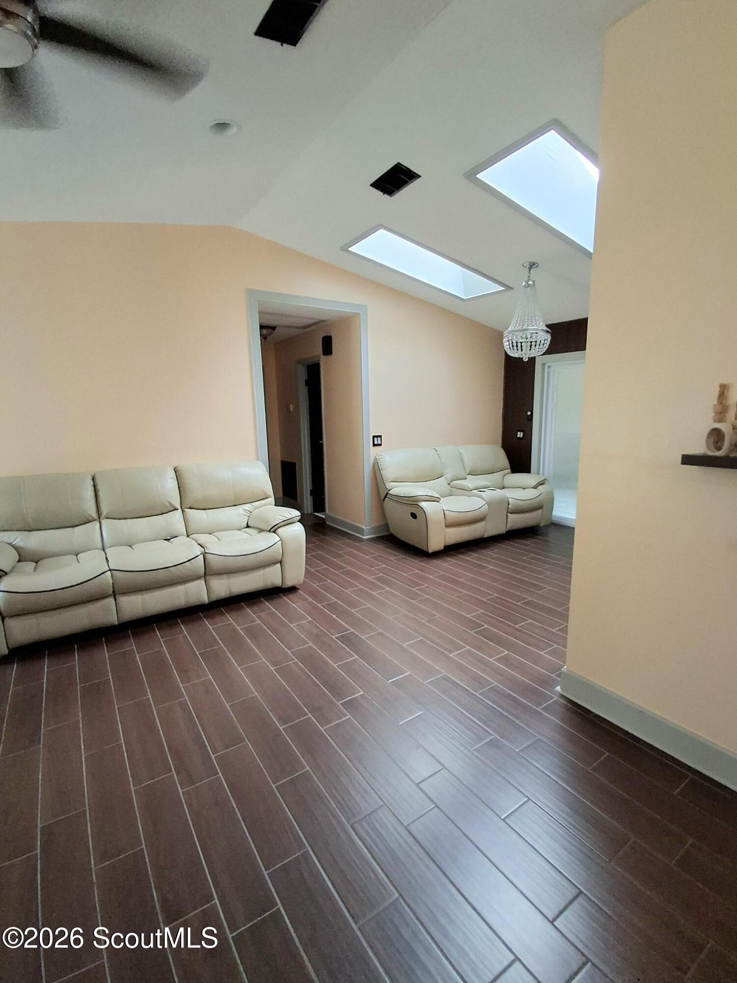 Furnished living room with cream reclining sofas, skylights, and dark tile flooring.