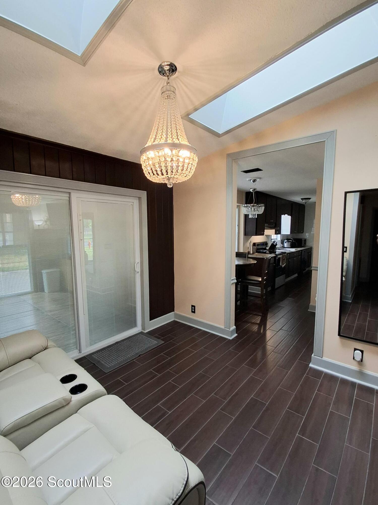 Living room with a crystal chandelier, skylights, and white sectional beside the adjoining kitchen.