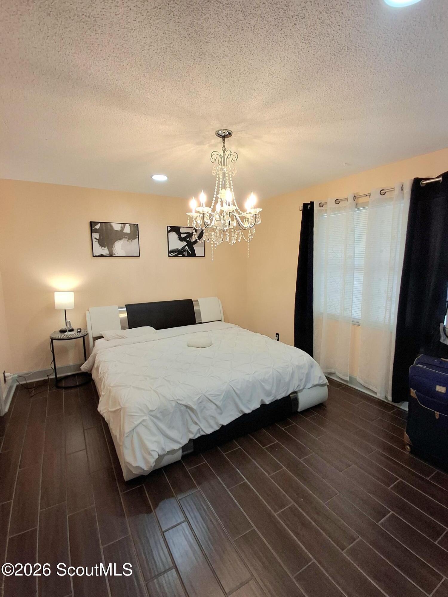 Bedroom with a crystal chandelier, large bed, and dark tile flooring.