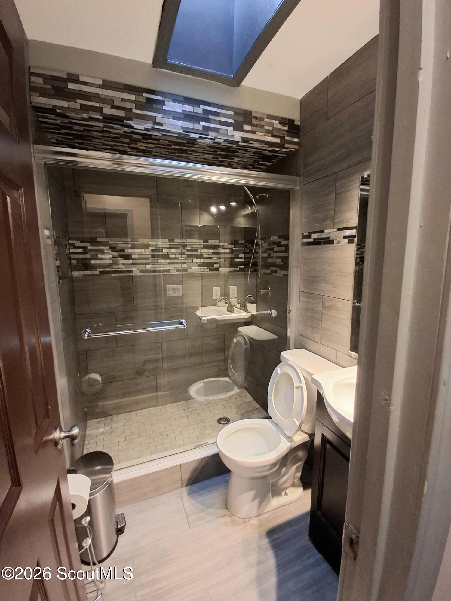 Modern tiled bathroom with a glass shower enclosure and skylight.