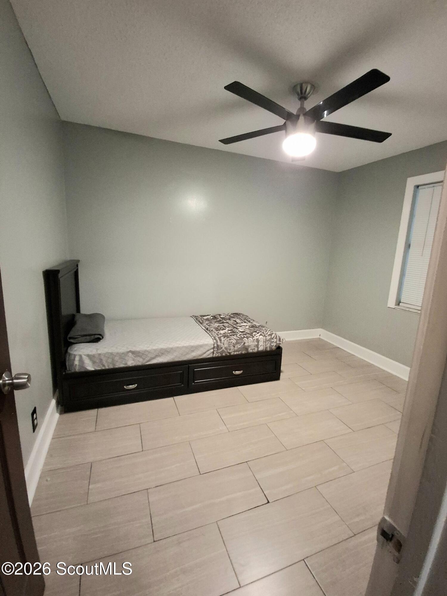 Bedroom with a dark storage bed, large beige tile floor, and ceiling fan.
