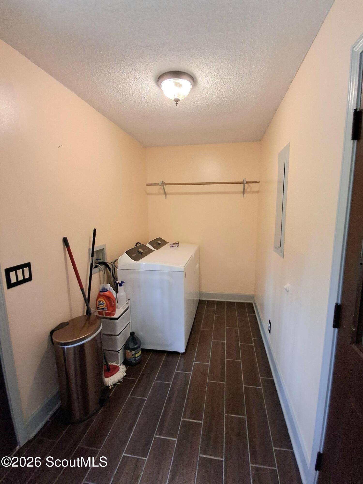 Laundry room with a top-loading washer, brown tile flooring, and a wall-mounted hanging rod.