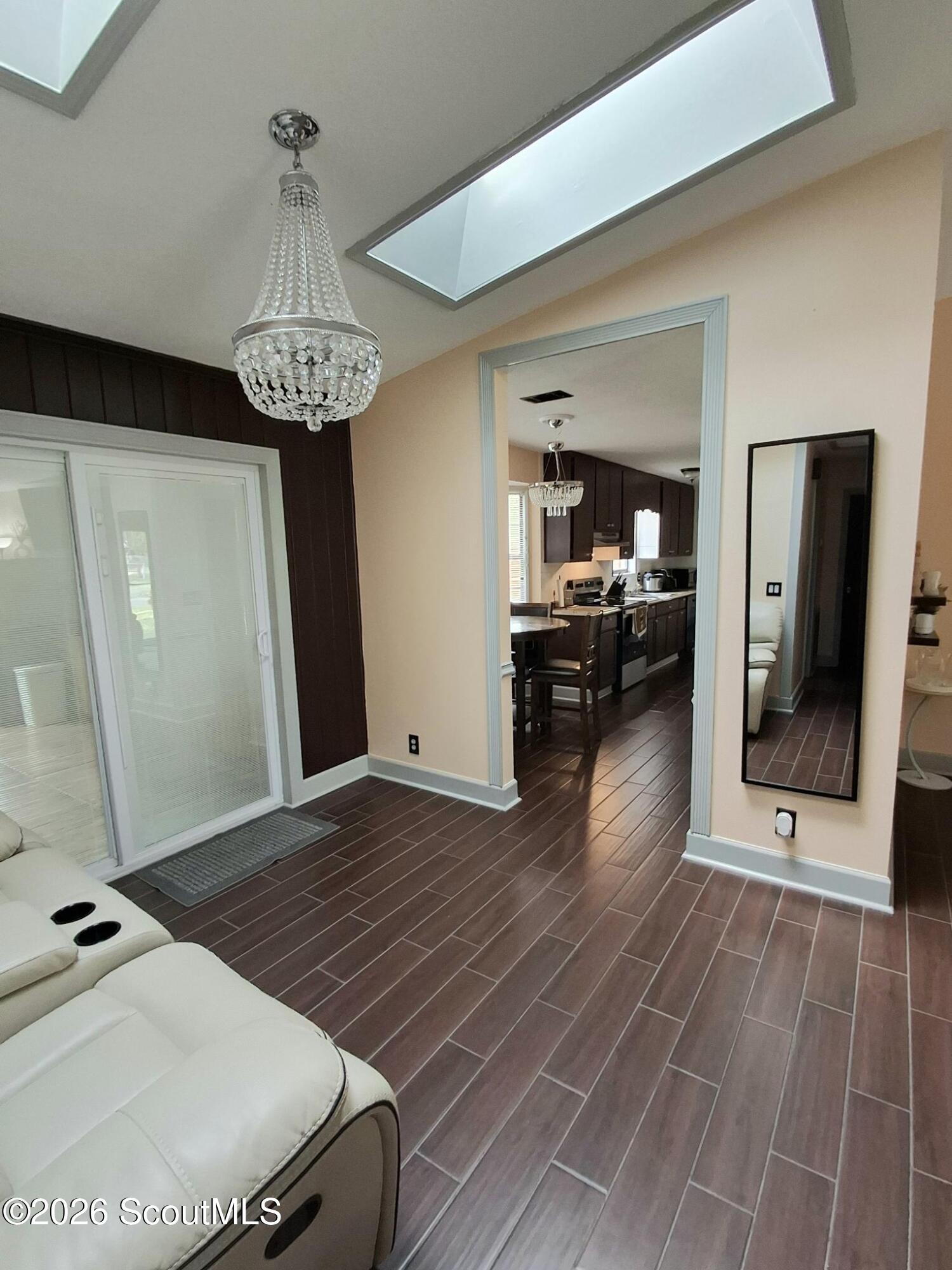 Living room with a crystal chandelier, skylights, and an open view into the kitchen.