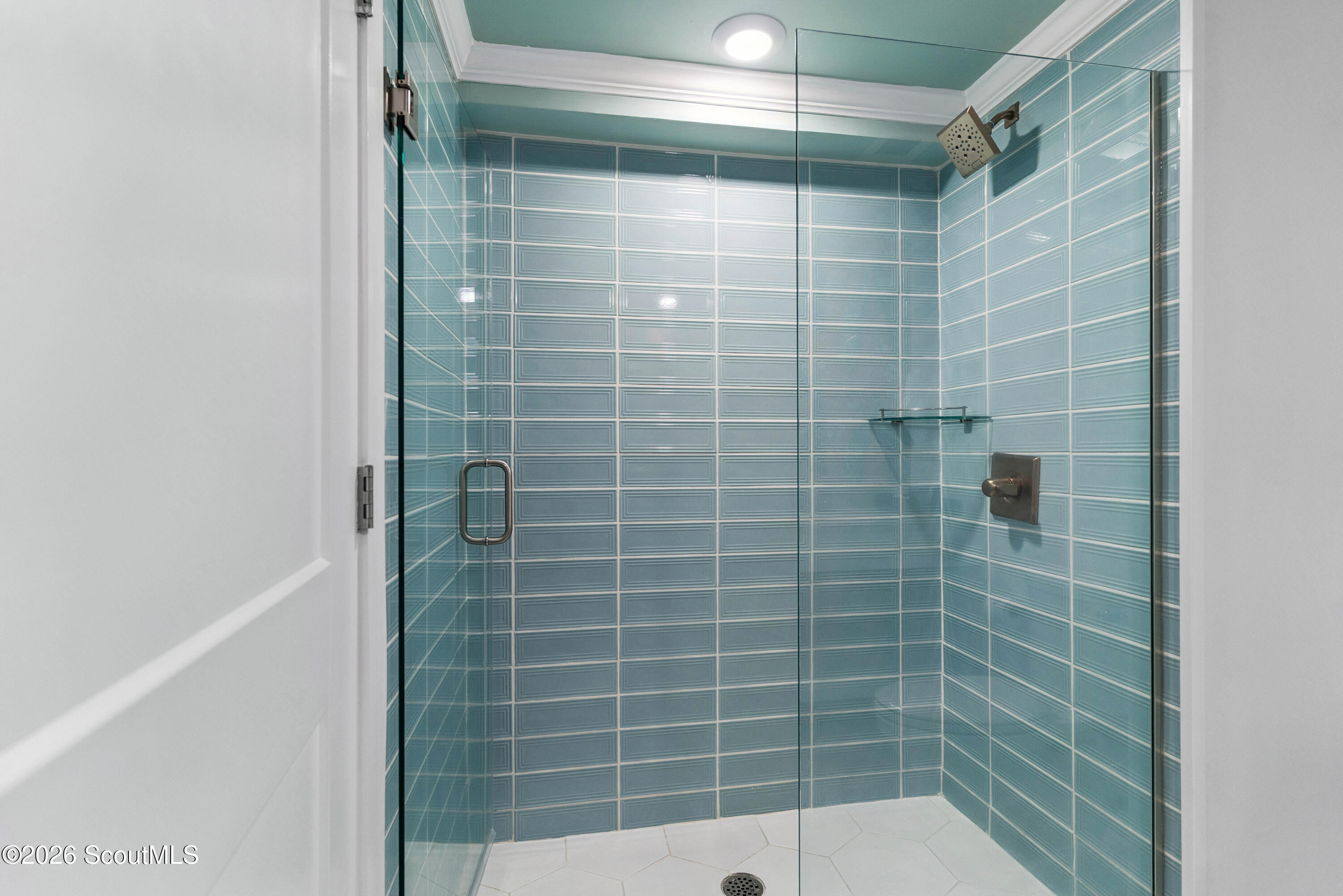 Walk-in shower with blue tile, clear glass enclosure, and white hexagonal floor tiles.