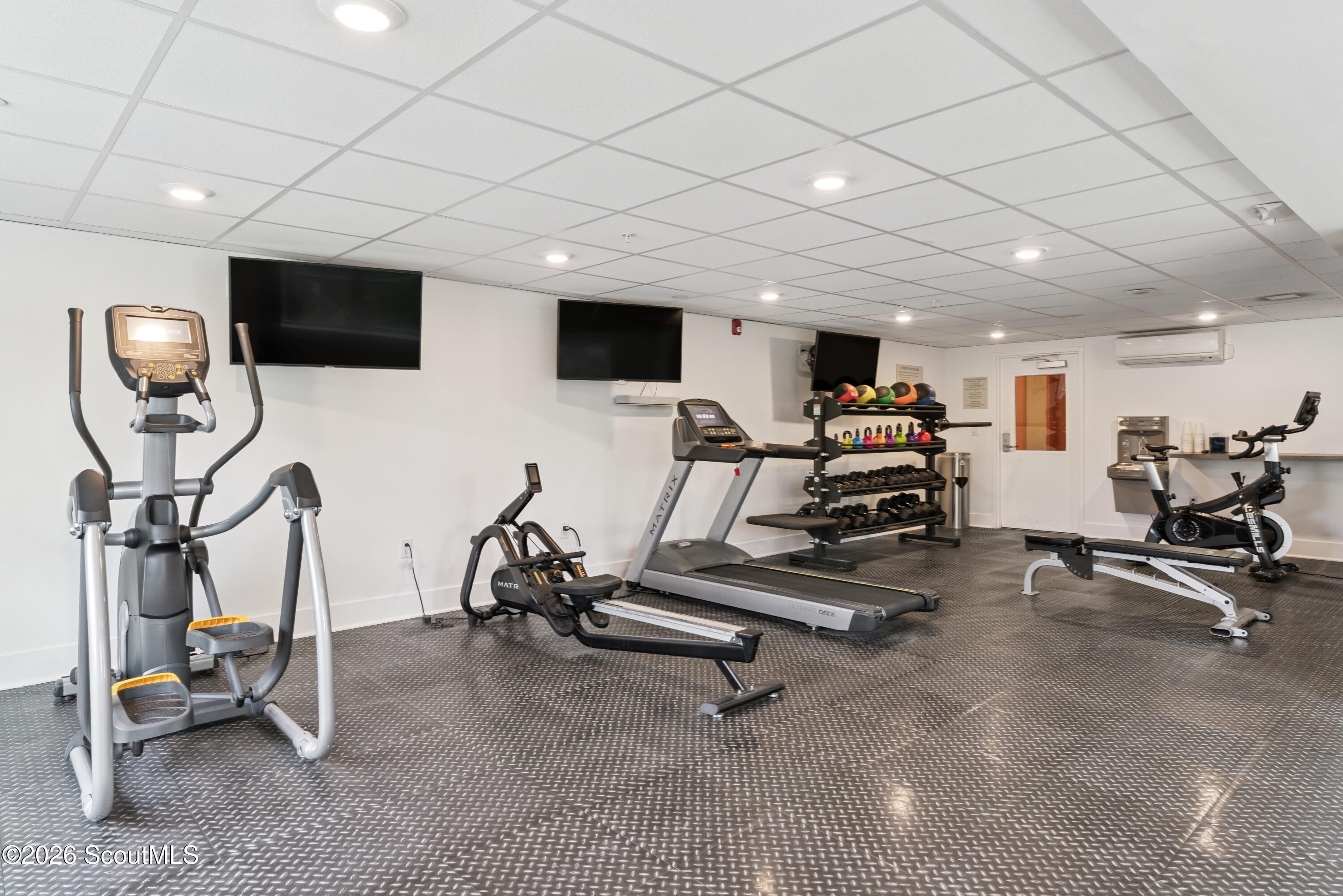Fitness center with cardio machines, free weights, medicine balls, and wall-mounted TVs.