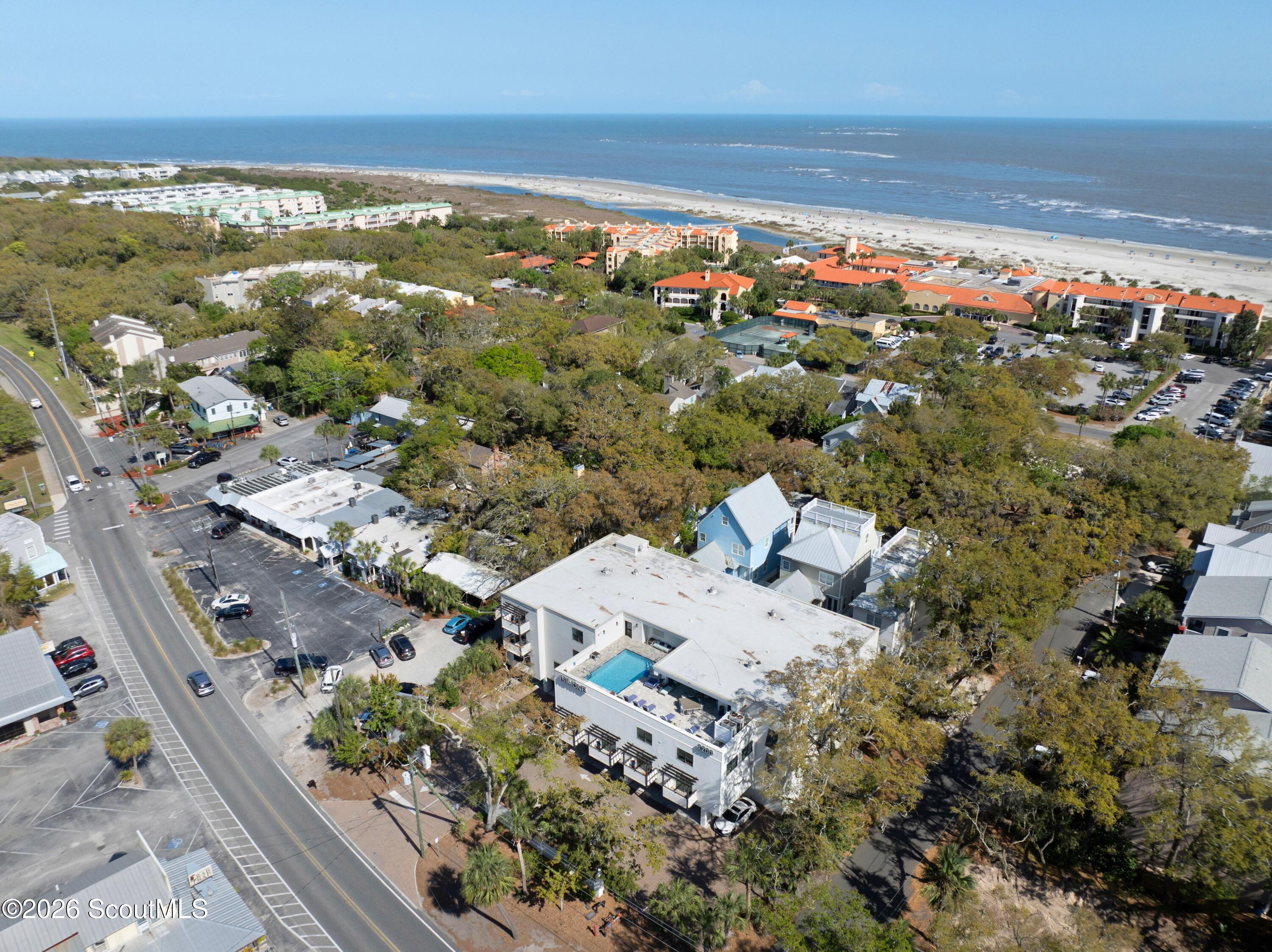 Aerial view of a coastal condominium and pool beside the beach, with the ocean beyond.