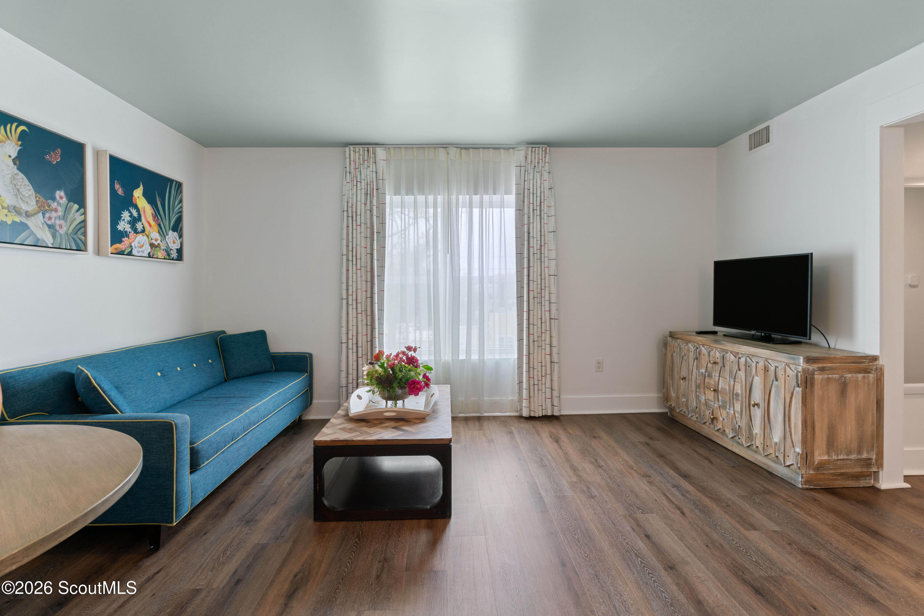Living room with a blue sofa, bird artwork, and television on a rustic wood console.