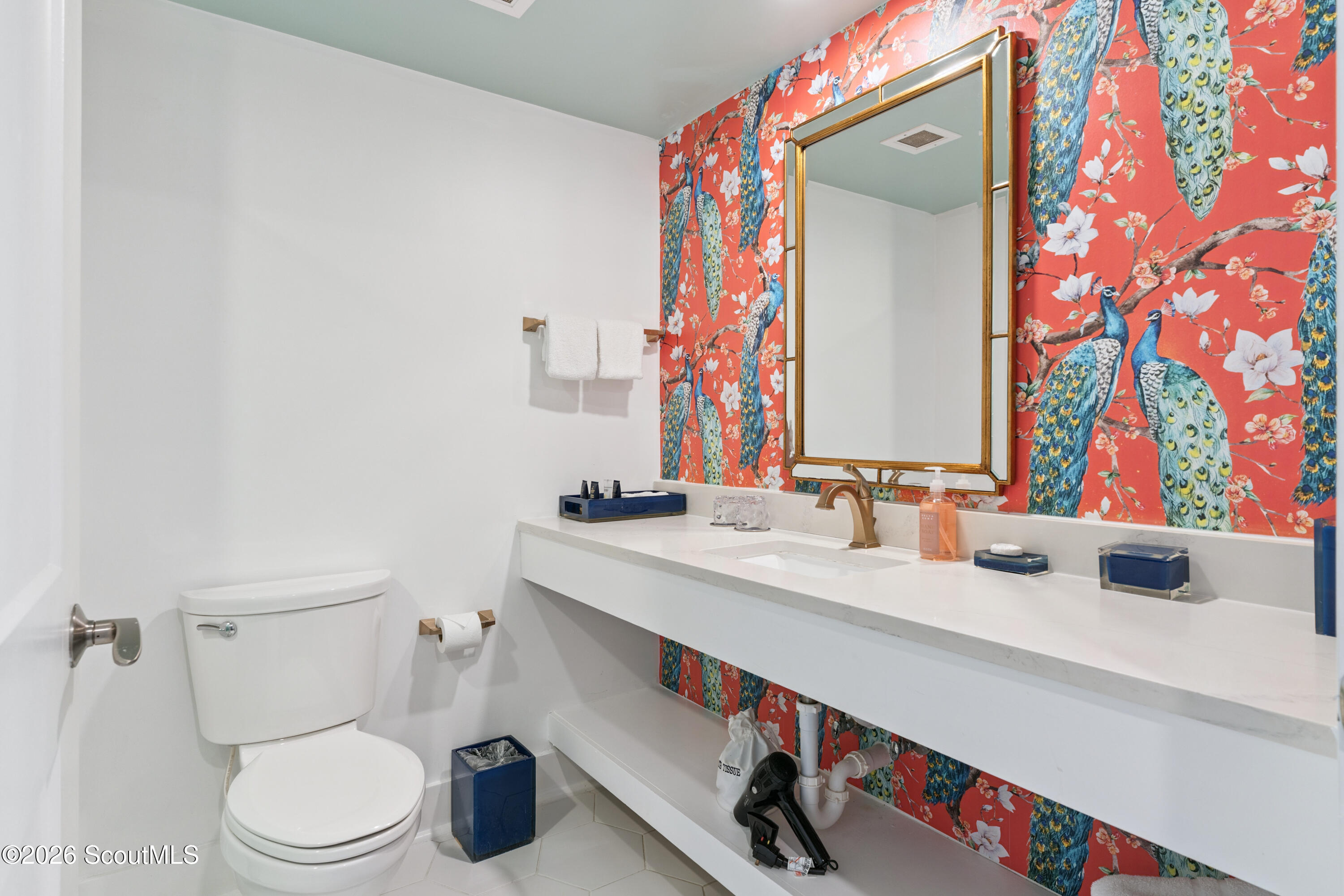 Bathroom with a floating vanity, gold-framed mirror, and vivid coral peacock-patterned wallpaper.