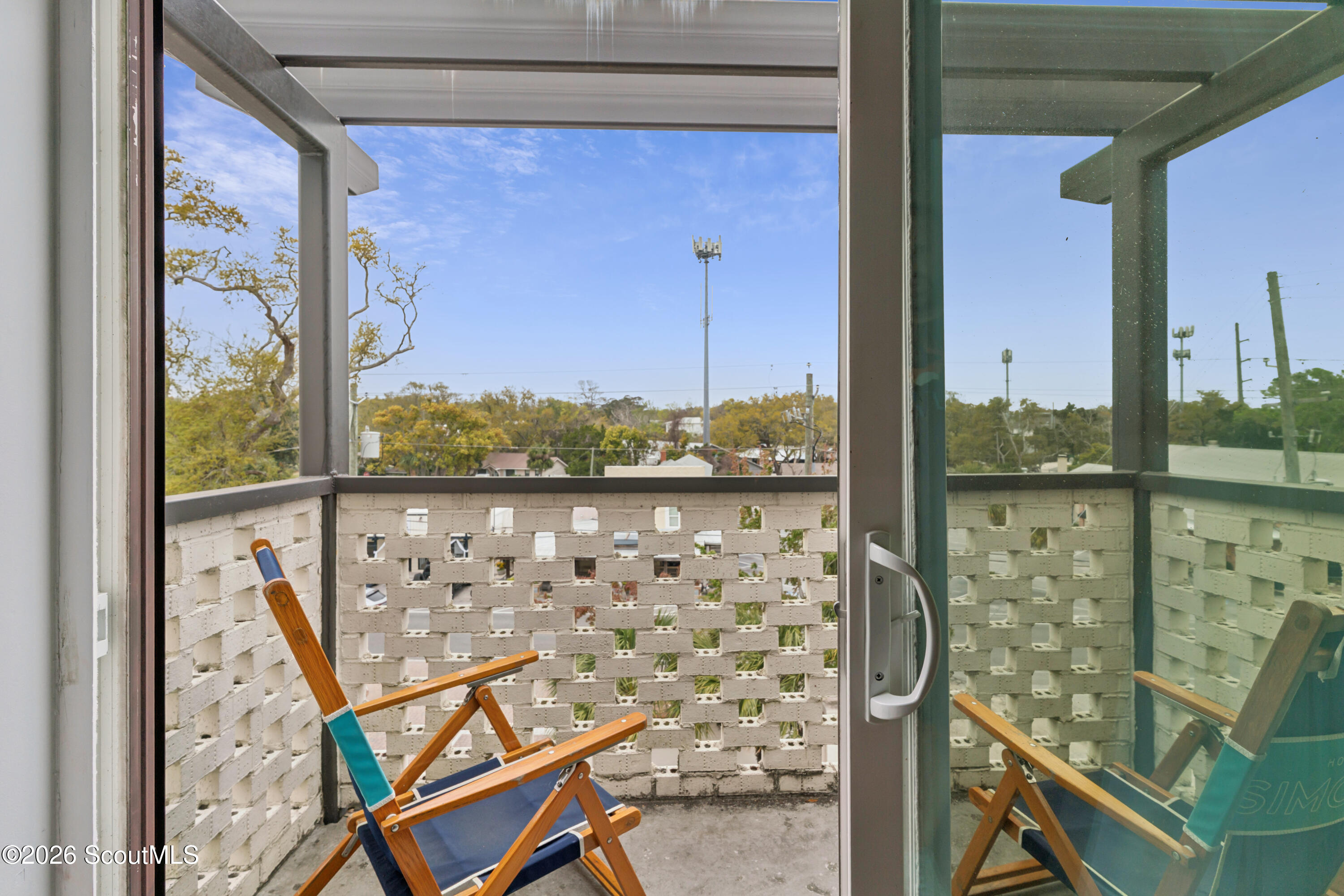 Covered balcony with a folding chair and white lattice railing overlooking treetops.
