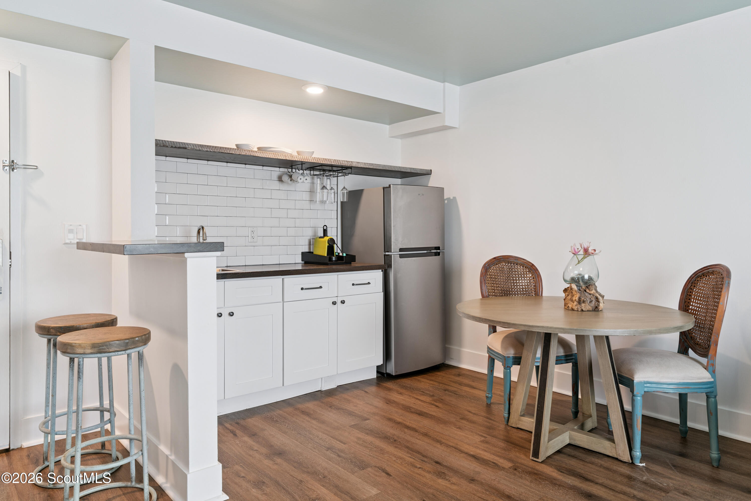 Kitchen and dining area with subway-tile backsplash, breakfast stools, and a round table with cane-back chairs.