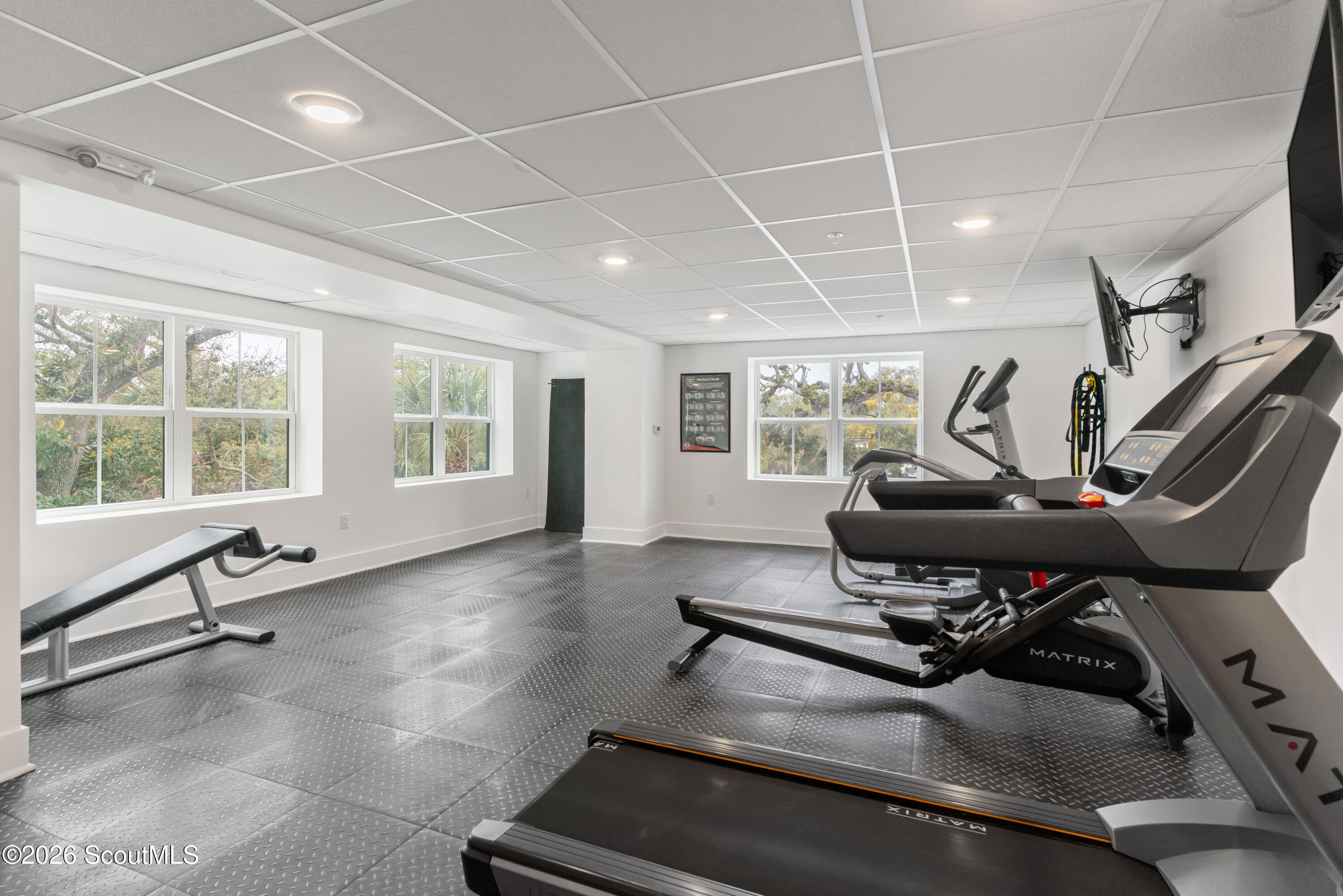 Fitness room with treadmills, an elliptical, and a weight bench beside large windows.