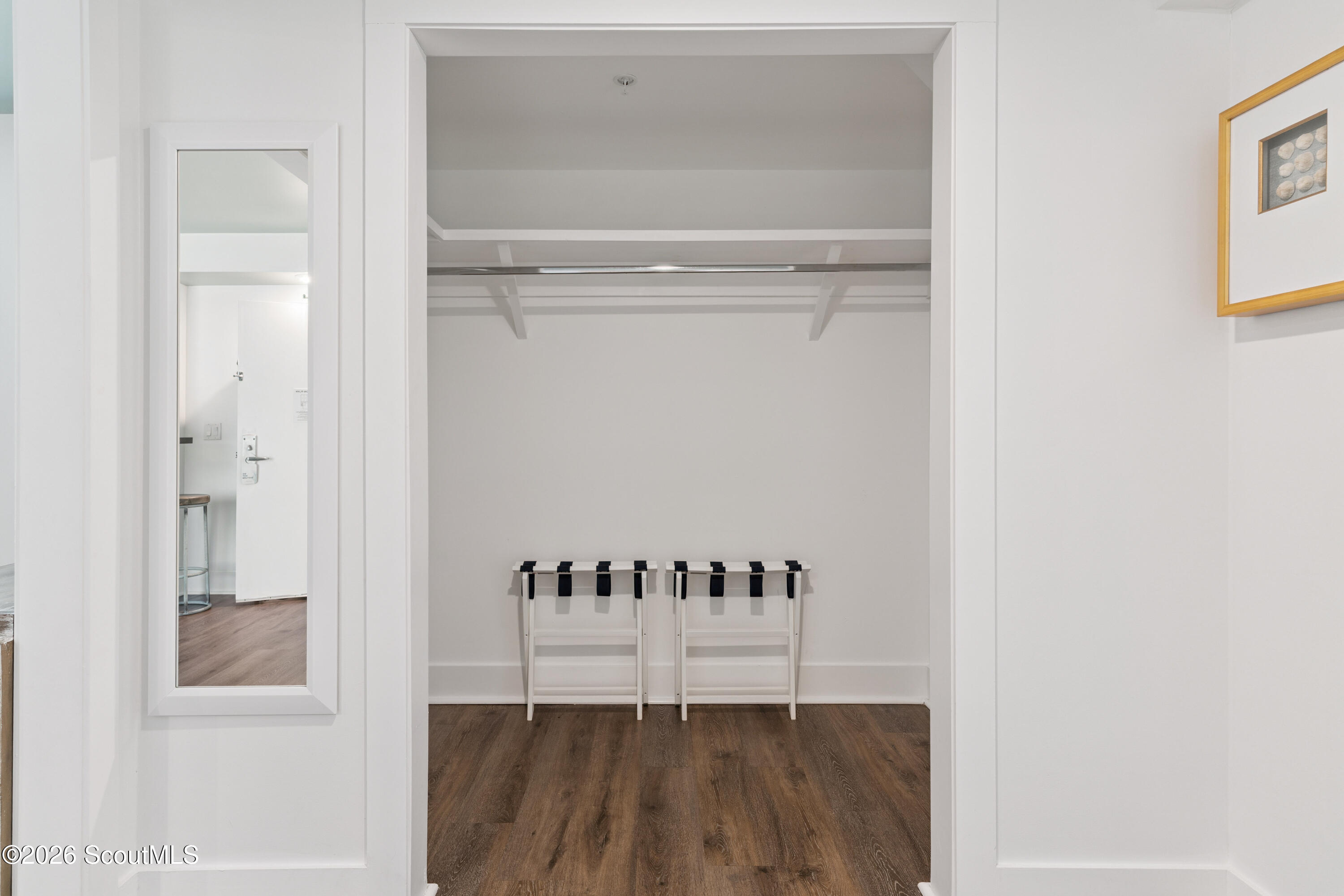 Walk-in closet with white built-in shelving, dark wood floors, and two luggage racks.