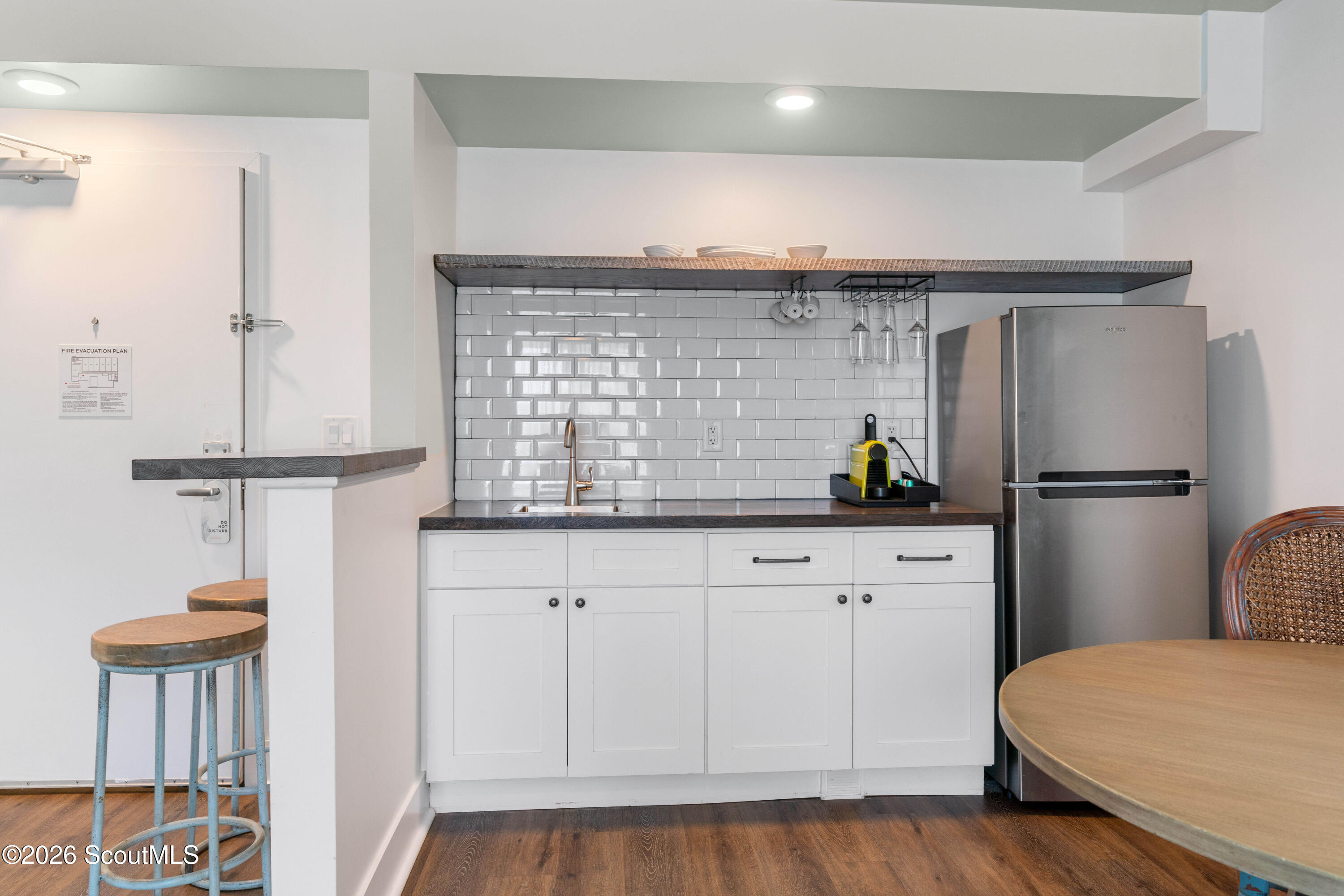 Condominium kitchen with white subway tile, stainless steel refrigerator, and stools at a breakfast bar.