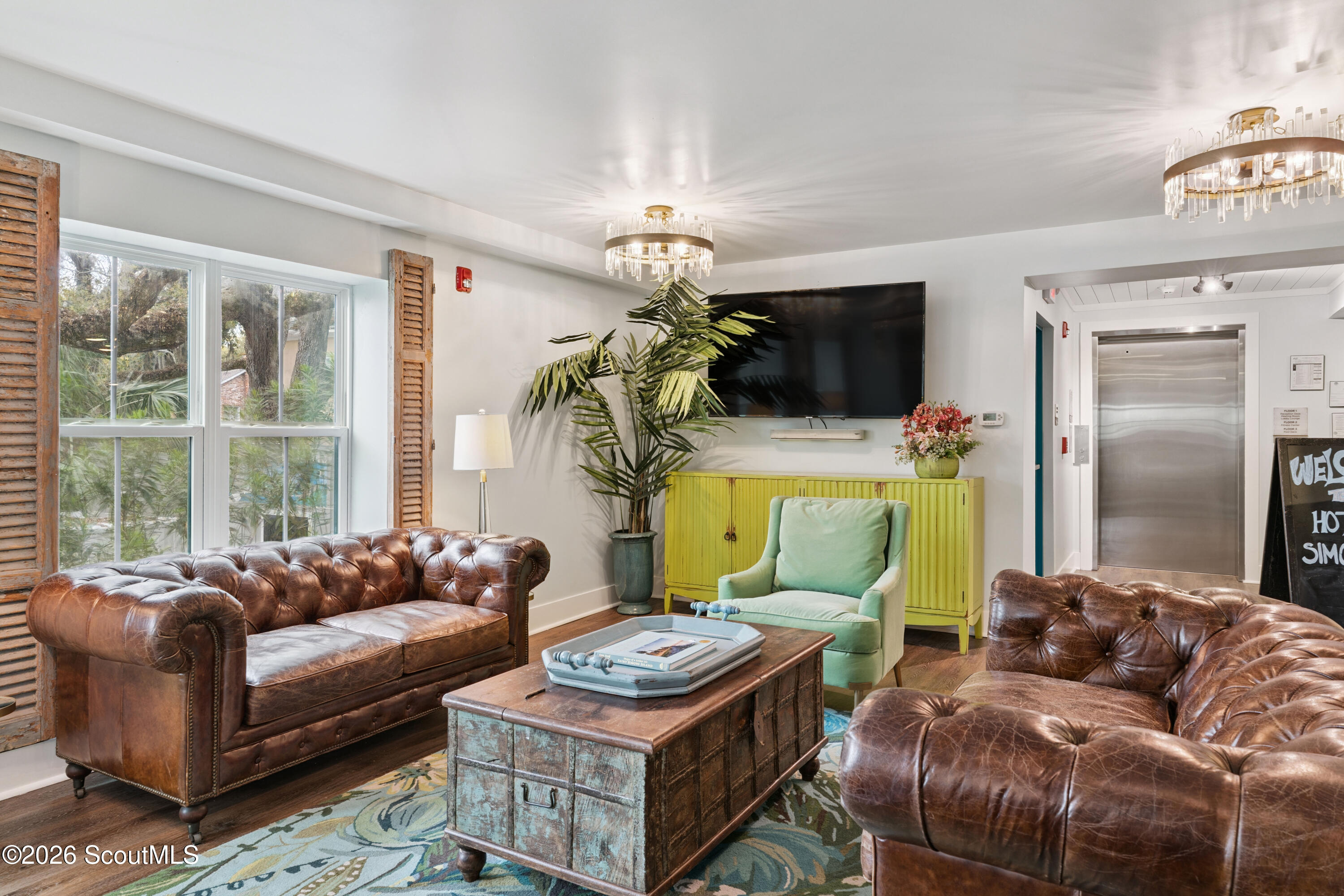Furnished lobby lounge with leather sofas, a pale green armchair, and an elevator.