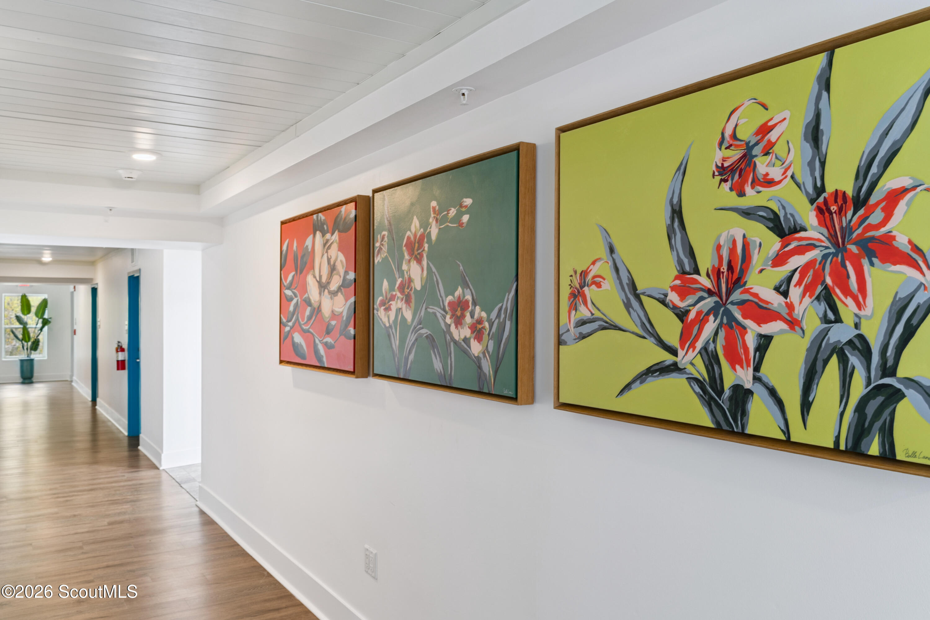 Interior hallway with three colorful floral paintings and light wood floors.