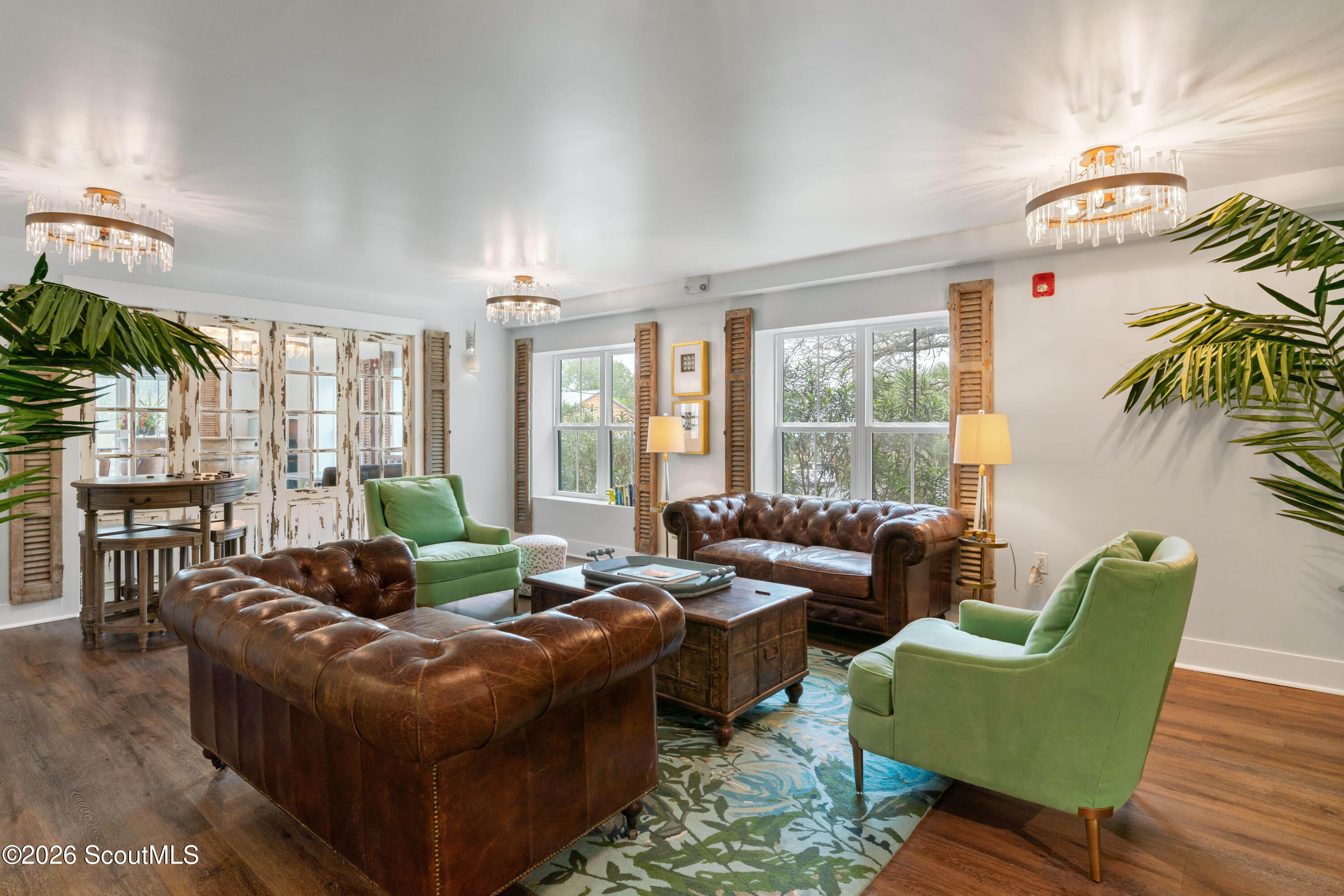 Living room with brown leather sofas, green armchairs, shuttered windows, and crystal ceiling lights.