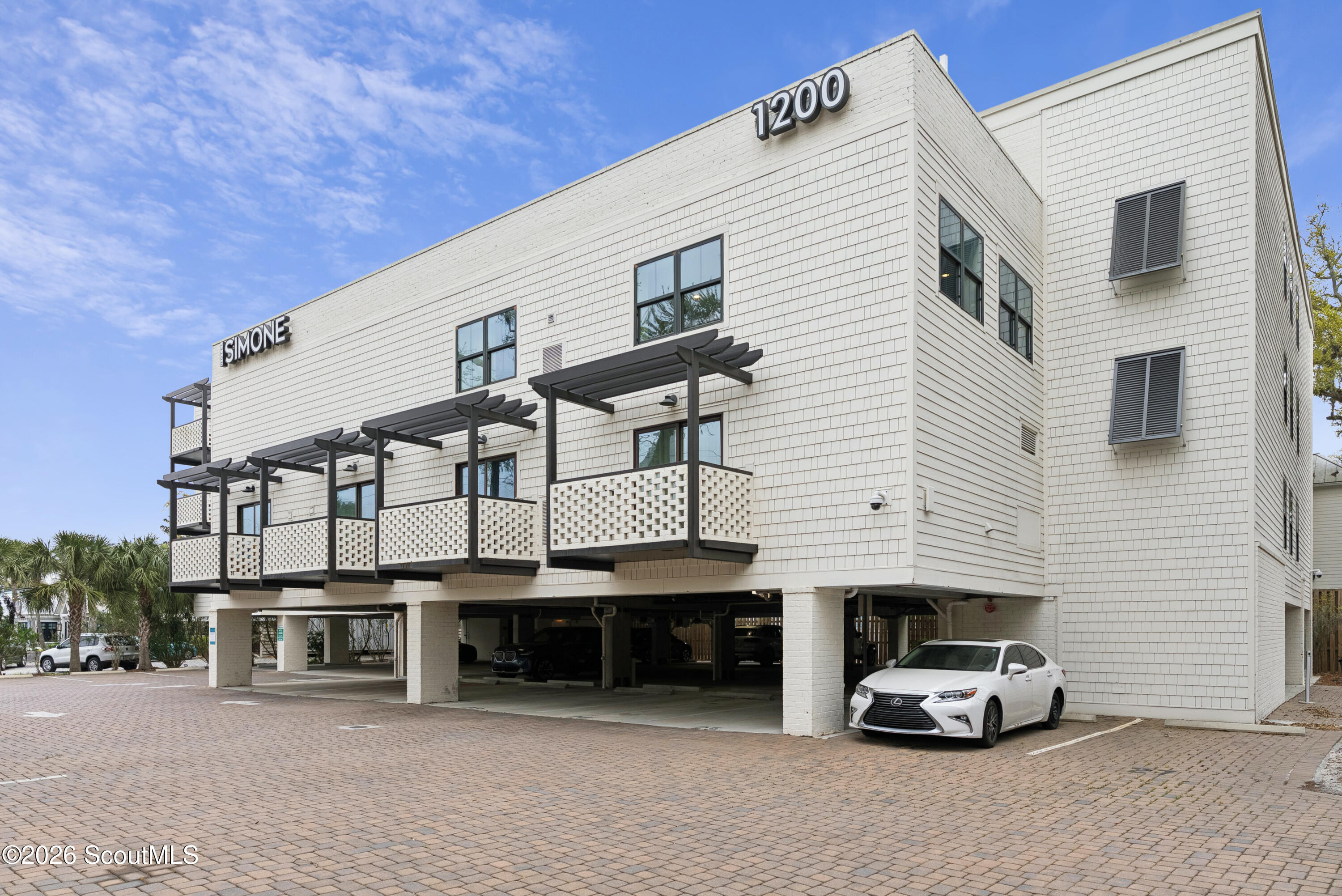 White multi-story building with balconies and covered parking, marked 1200 and SIMONE.