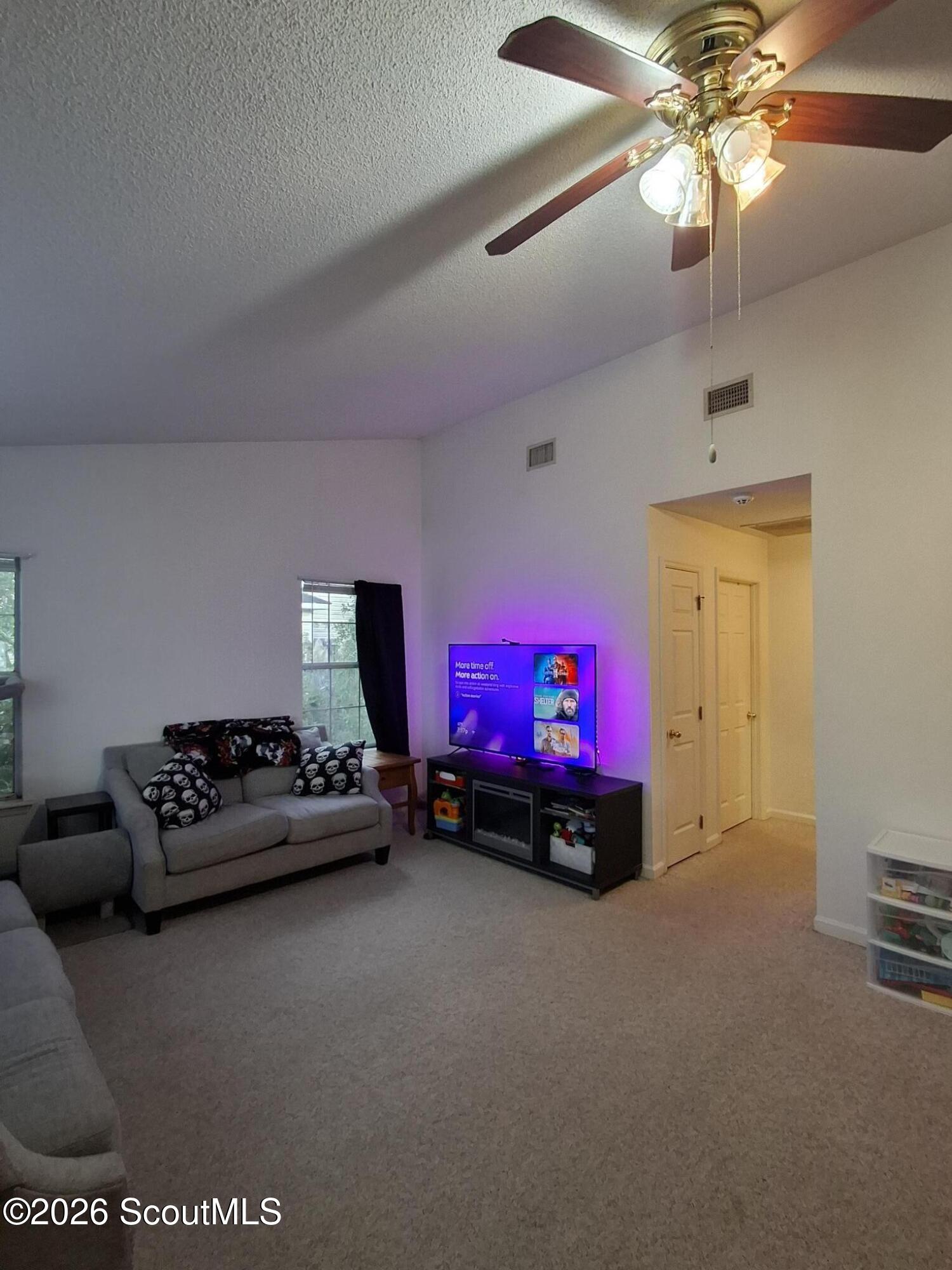 Living room with gray sofas, carpet, a ceiling fan, and a television glowing purple.