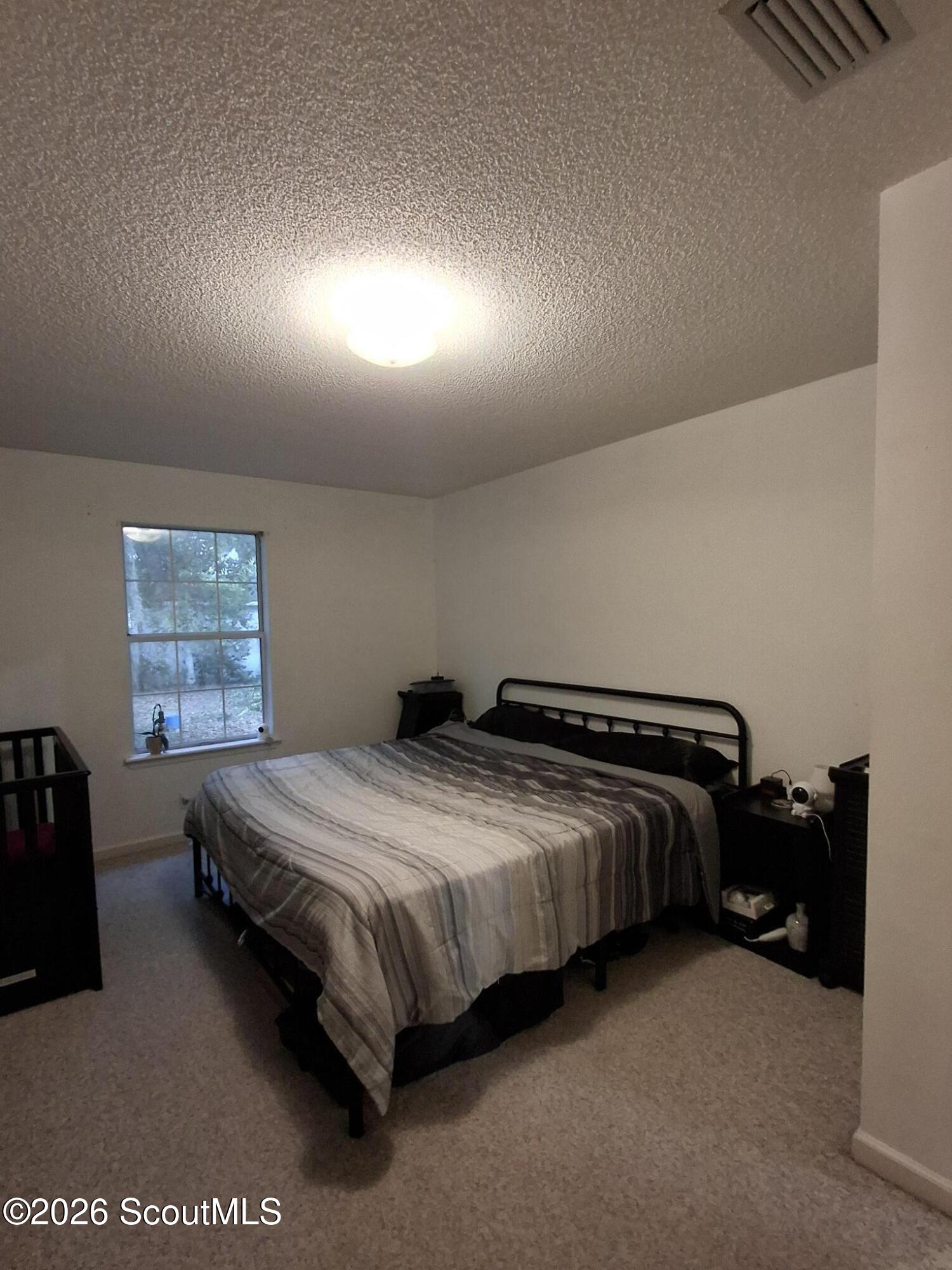 Bedroom with a black metal bed, gray striped bedding, carpet, and a single window.