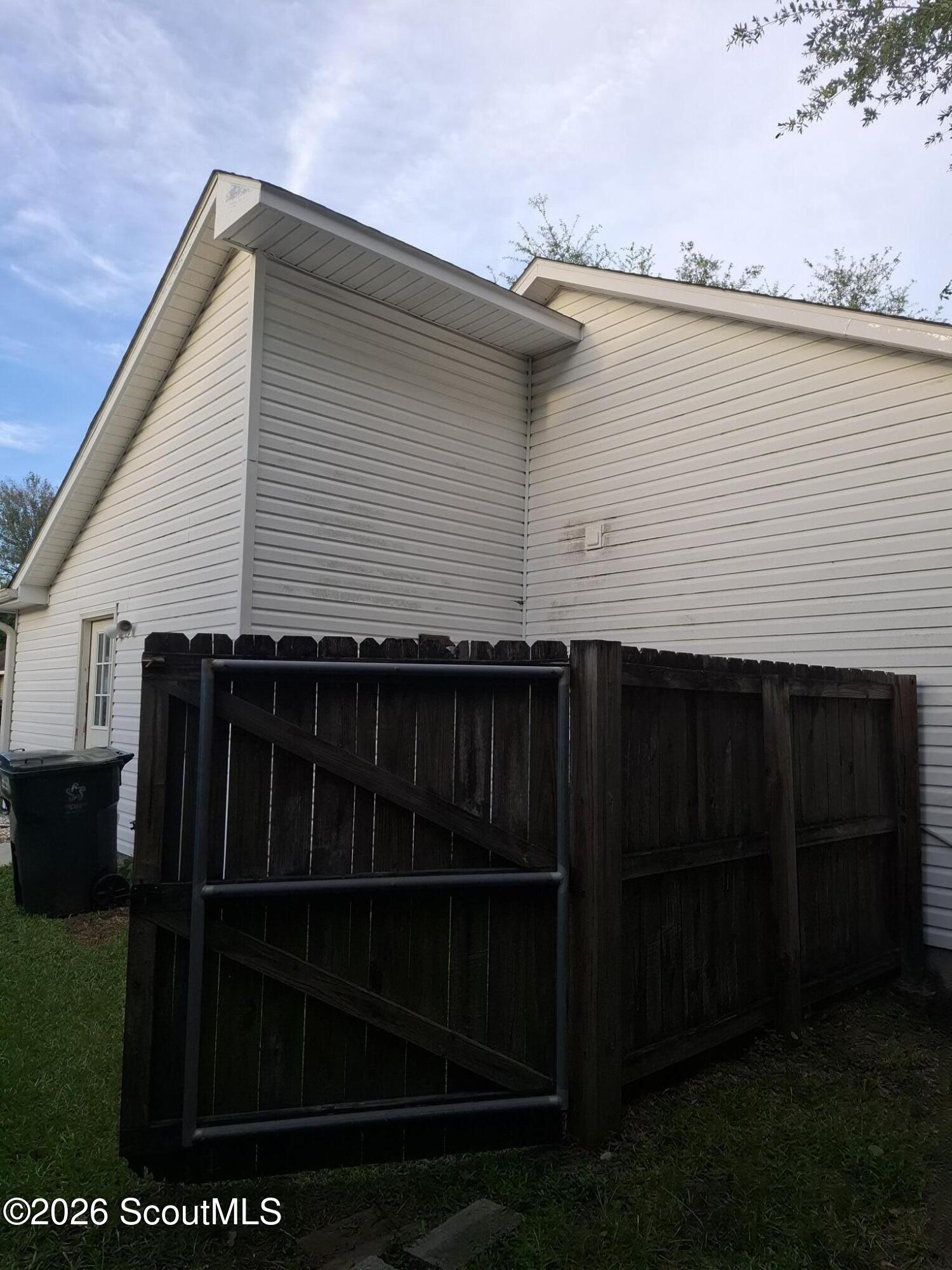 House exterior with light siding and a dark wooden fenced enclosure with a metal-framed gate.