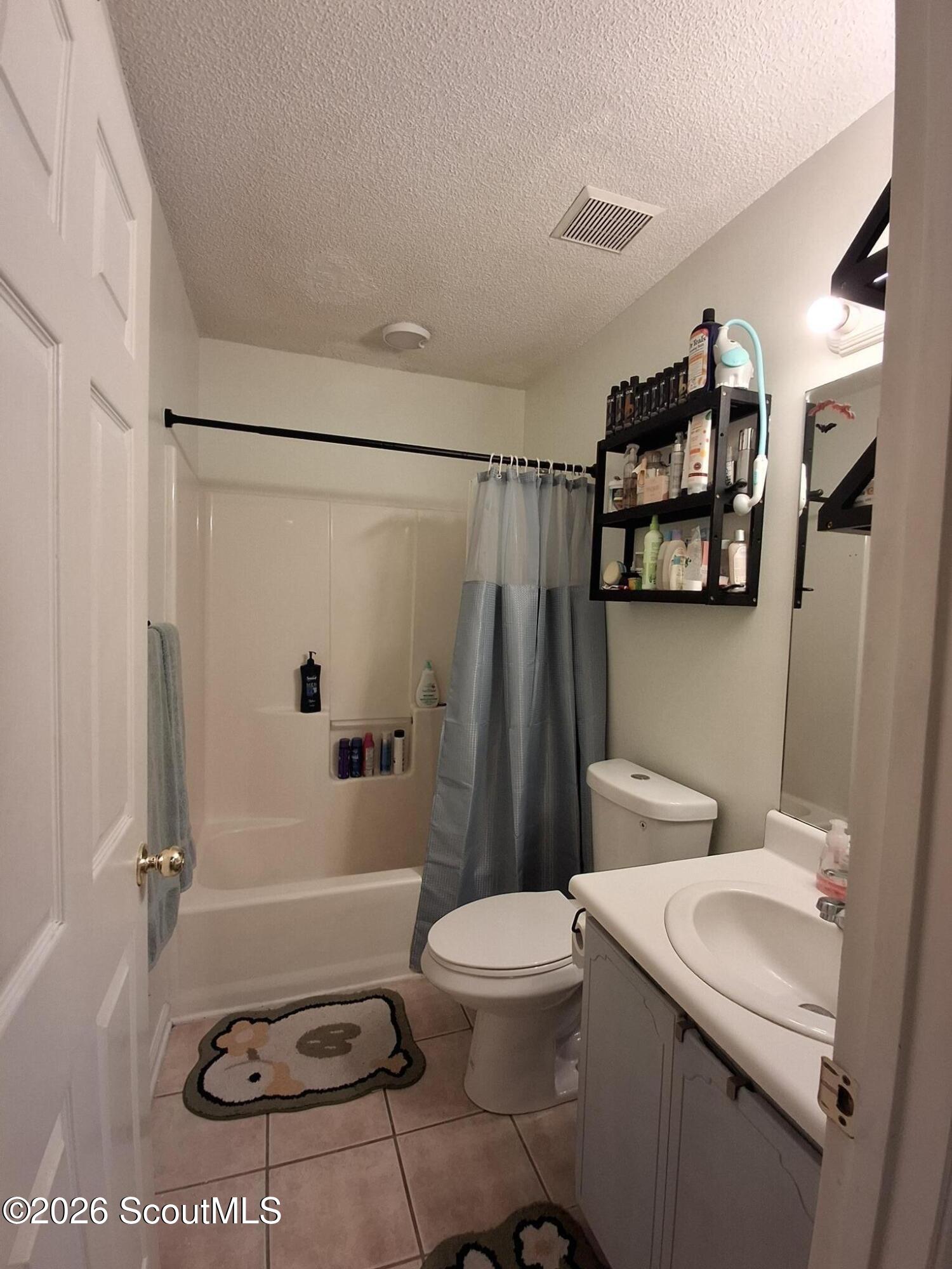 Bathroom with a tub, blue-gray shower curtain, toilet, and white vanity with sink.