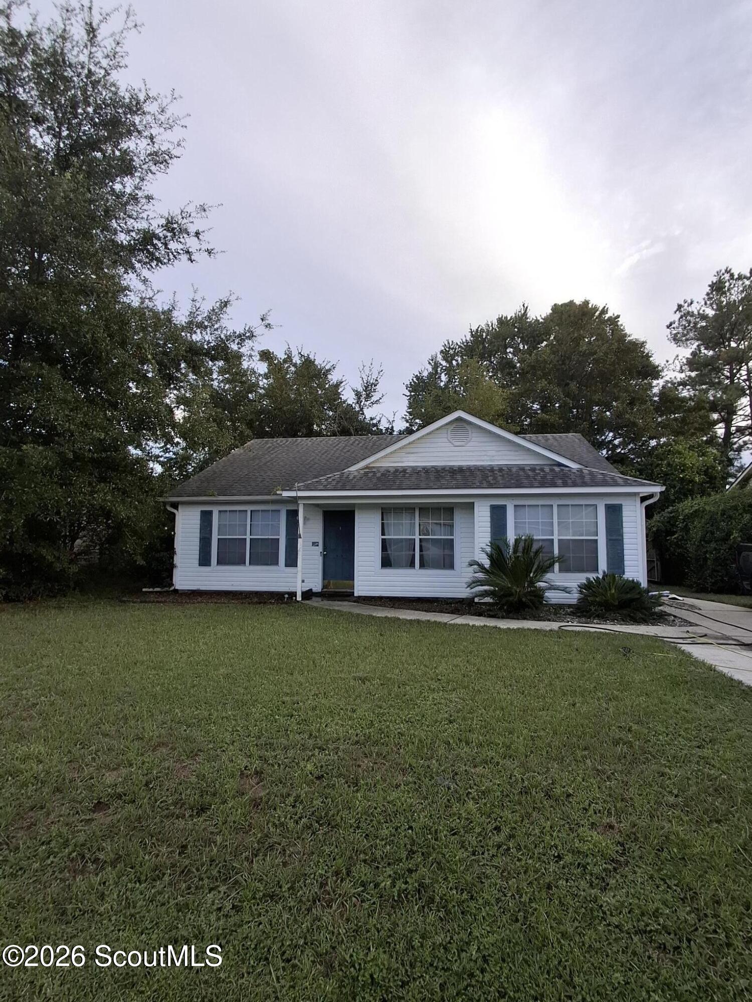 Single-story white house with blue shutters, a broad front lawn, and mature trees.
