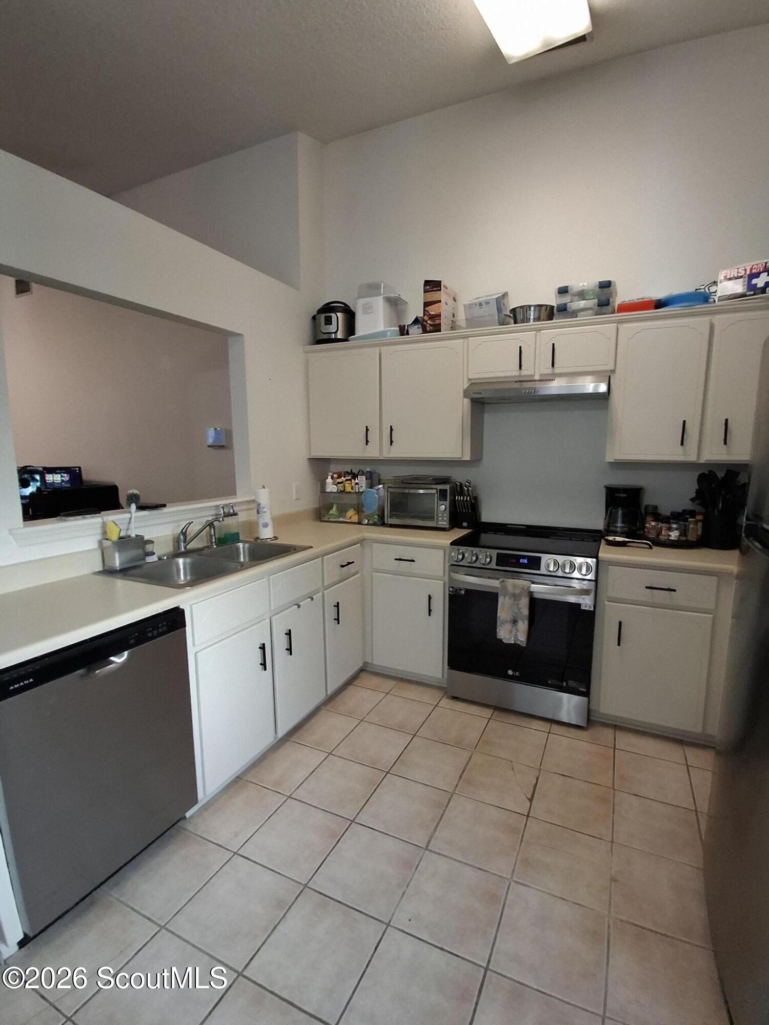 Kitchen with white cabinets, stainless steel appliances, tiled floor, and a pass-through opening.