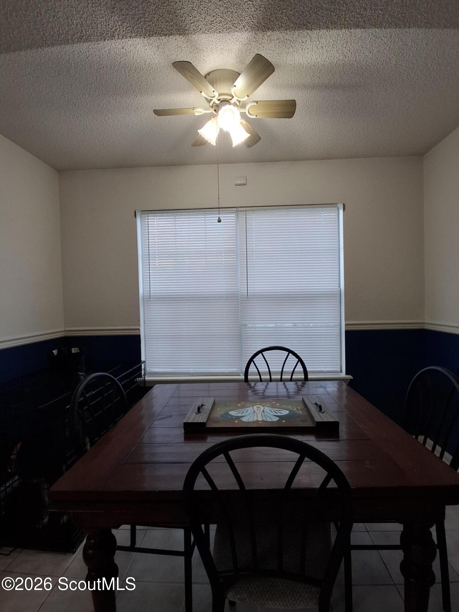 Dining room with a dark wooden table, black chairs, closed window blinds, and a lit ceiling fan.