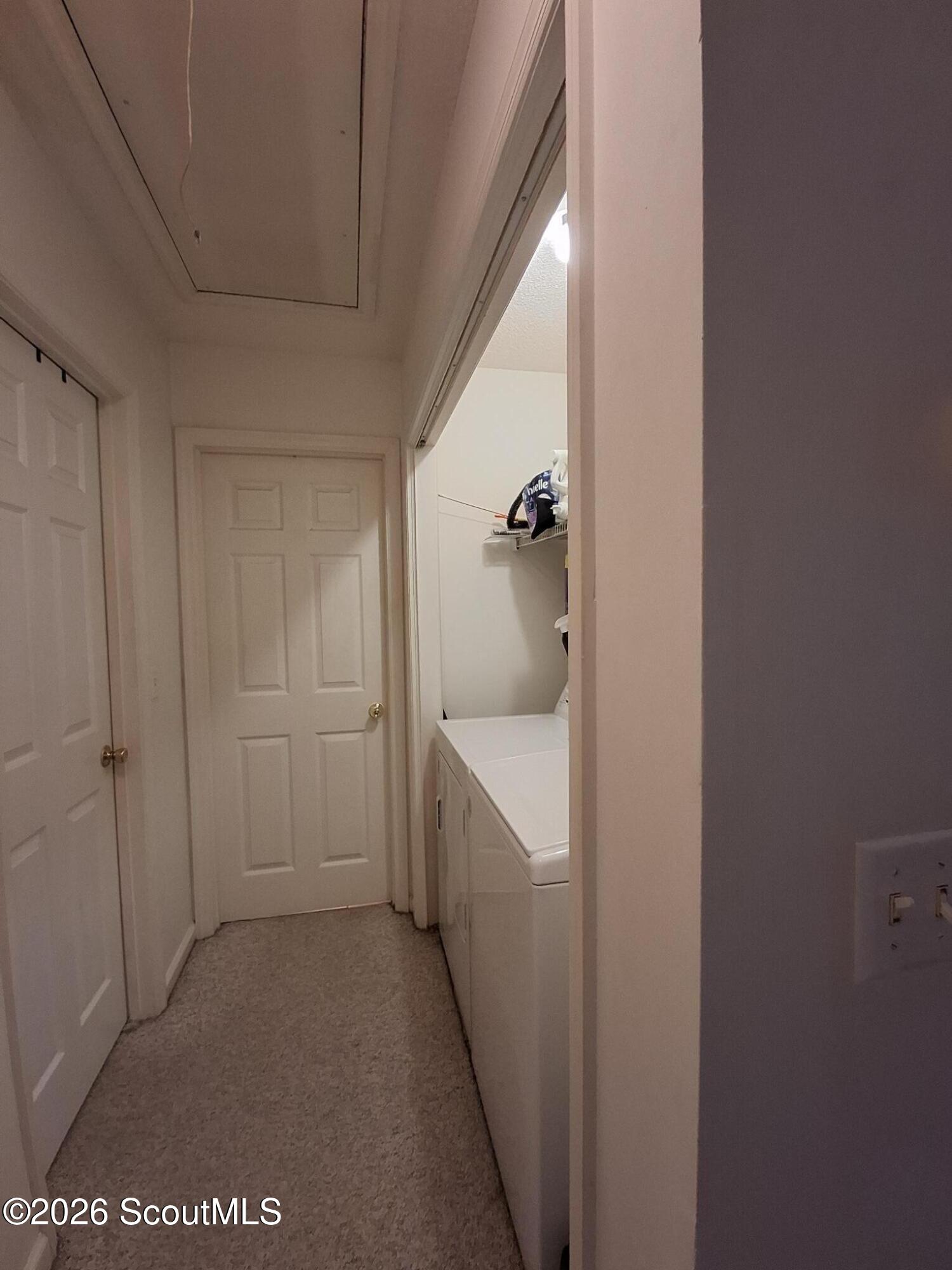 Laundry area with a white washer and dryer beside a narrow carpeted hallway.