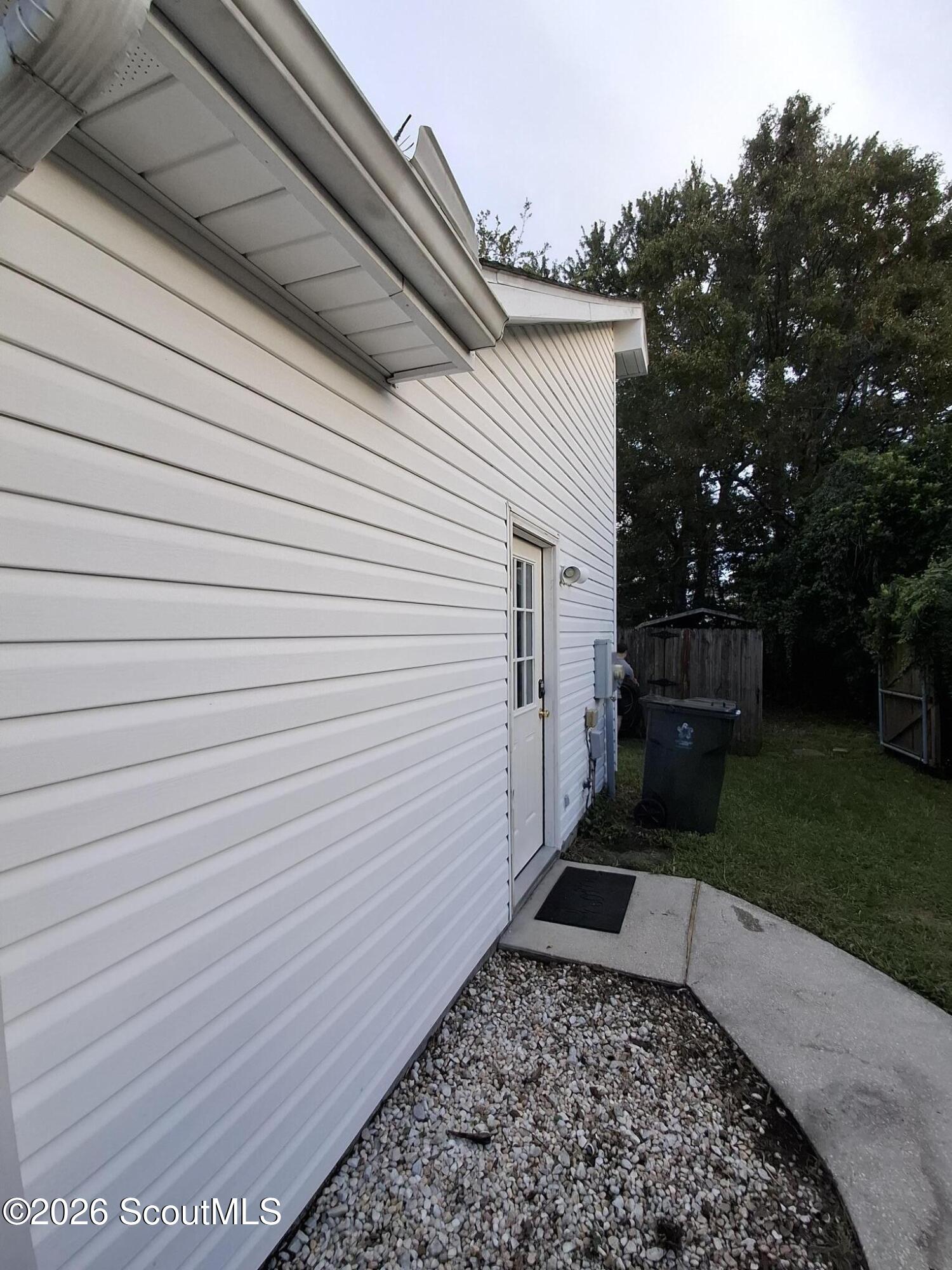 White-sided house with a glass-paneled side door, gravel border, and walkway beside a grassy yard.