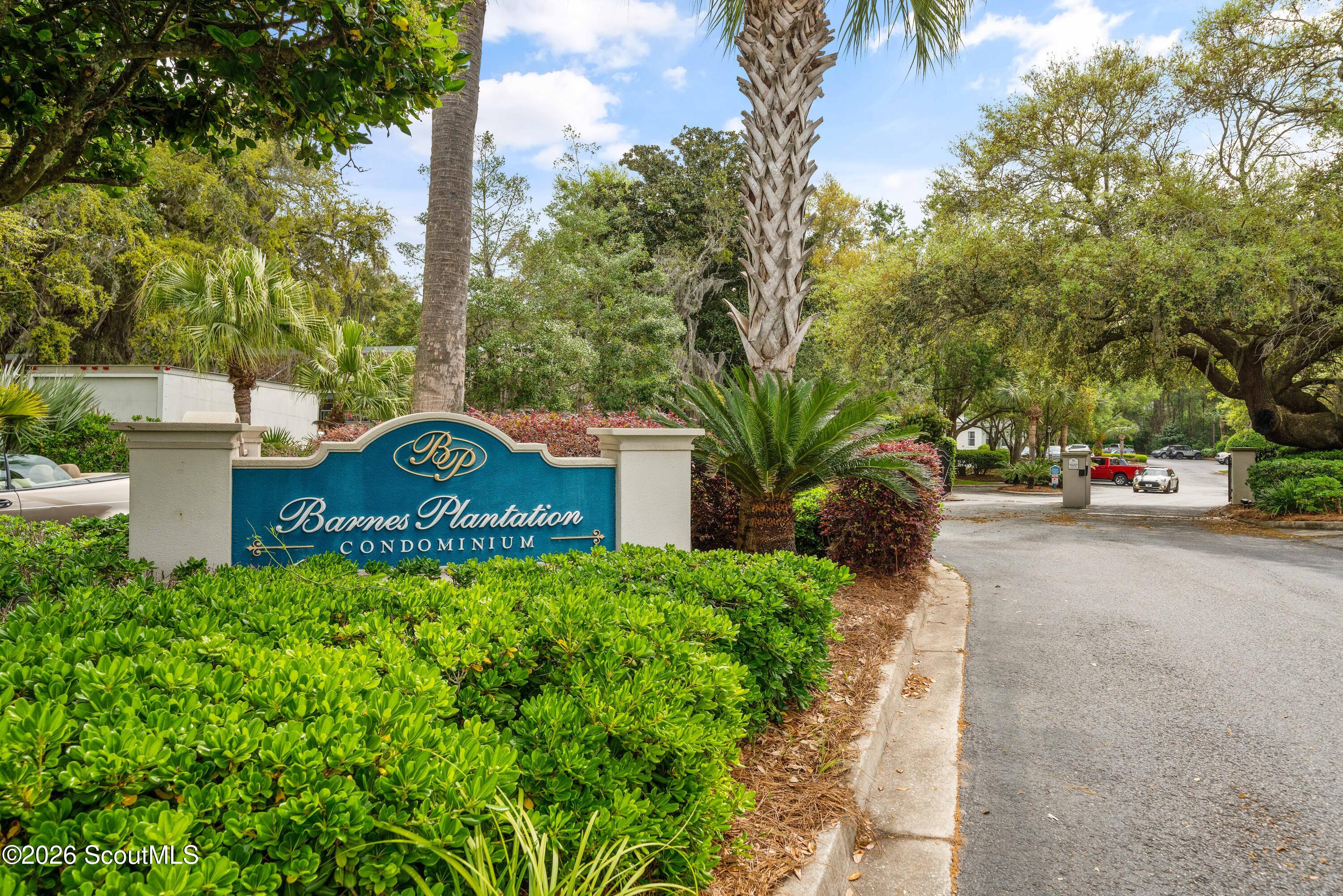 Barnes Plantation Condominium entrance sign amid palms and lush landscaping.