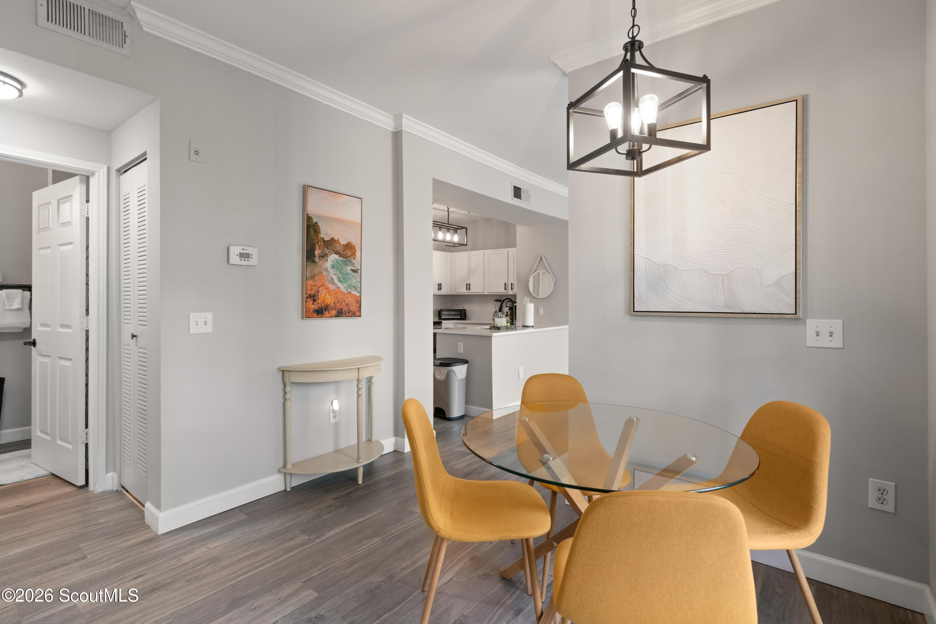 Dining area with a glass-top table, mustard-yellow chairs, and an open kitchen.