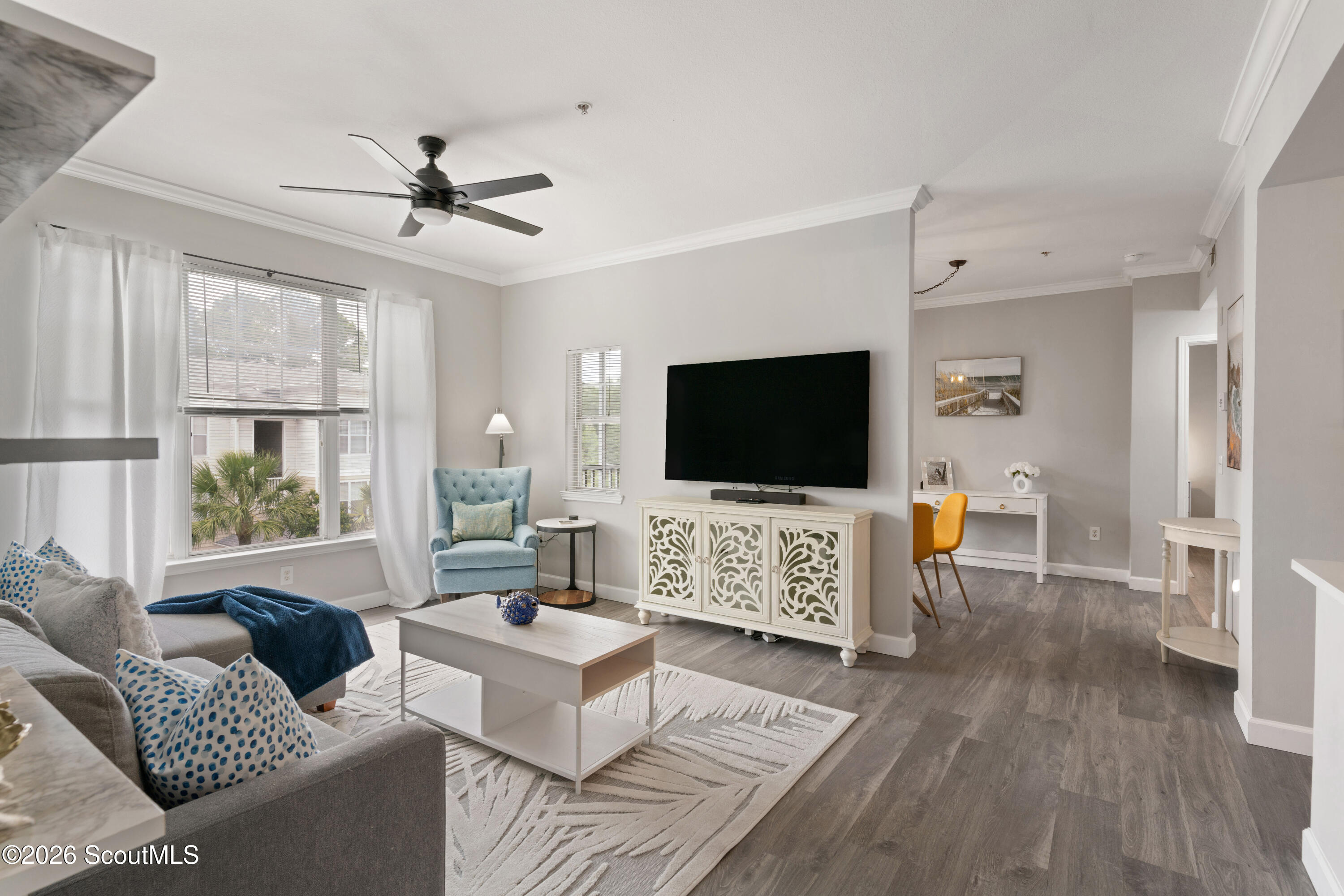 Furnished living room with blue accents, a large television, and an adjoining dining area.